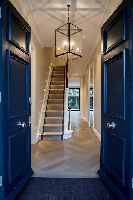 View of a modern entryway with blue double doors, a staircase with beige carpet, and a hexagonal chandelier hanging from the ceiling.