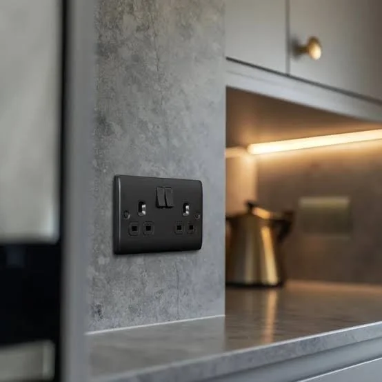 Close-up of a black electrical outlet and switch on a gray textured wall in a modern kitchen.