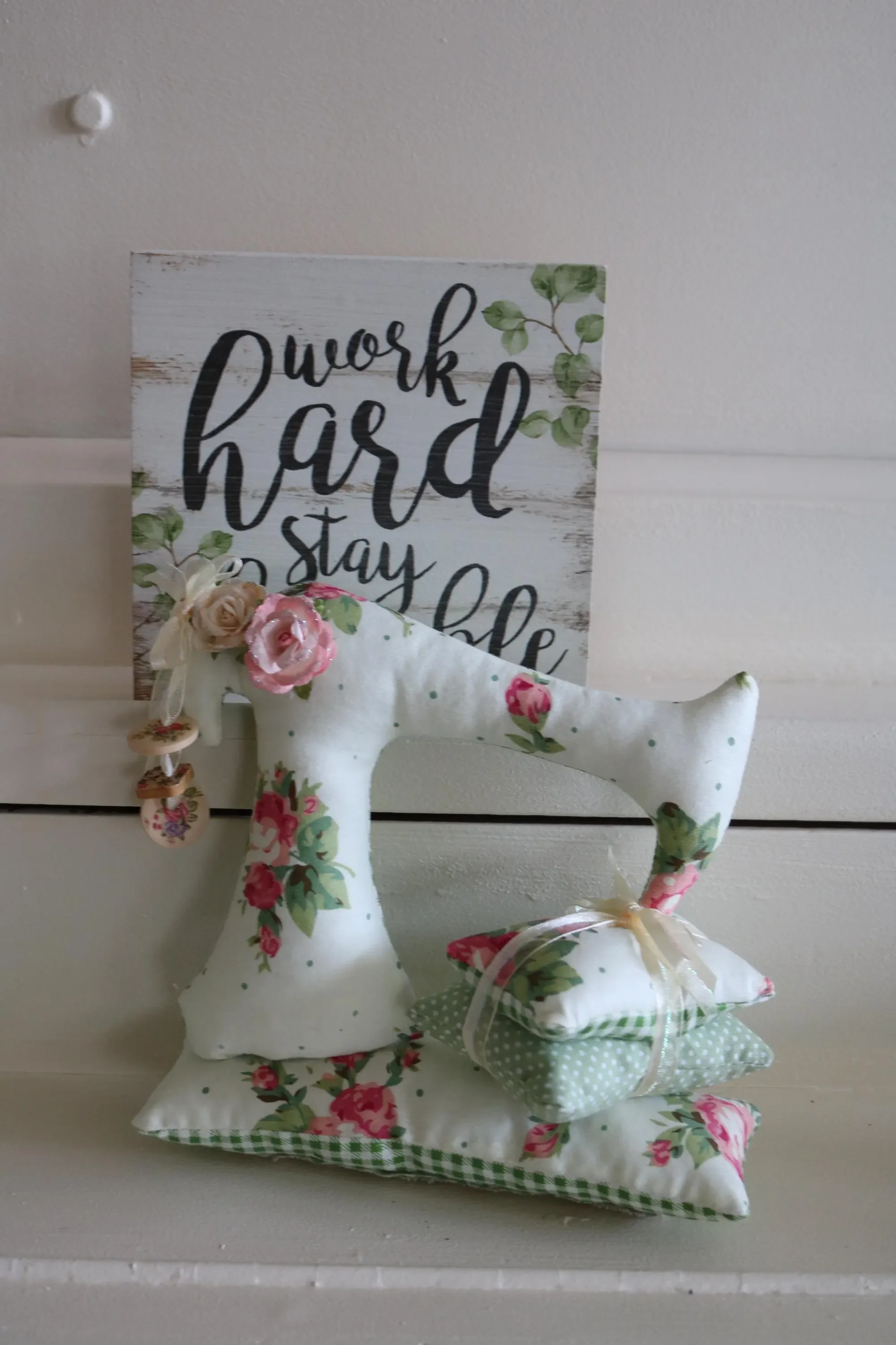 Decorative fabric sewn sewing machine with a Shabby Chic sign that says 'work hard stay kind' on a white shelf.