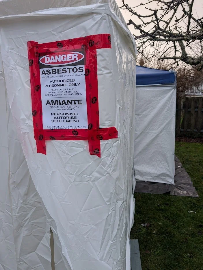 A white enclosure with a warning sign indicating asbestos, authorized personnel only.