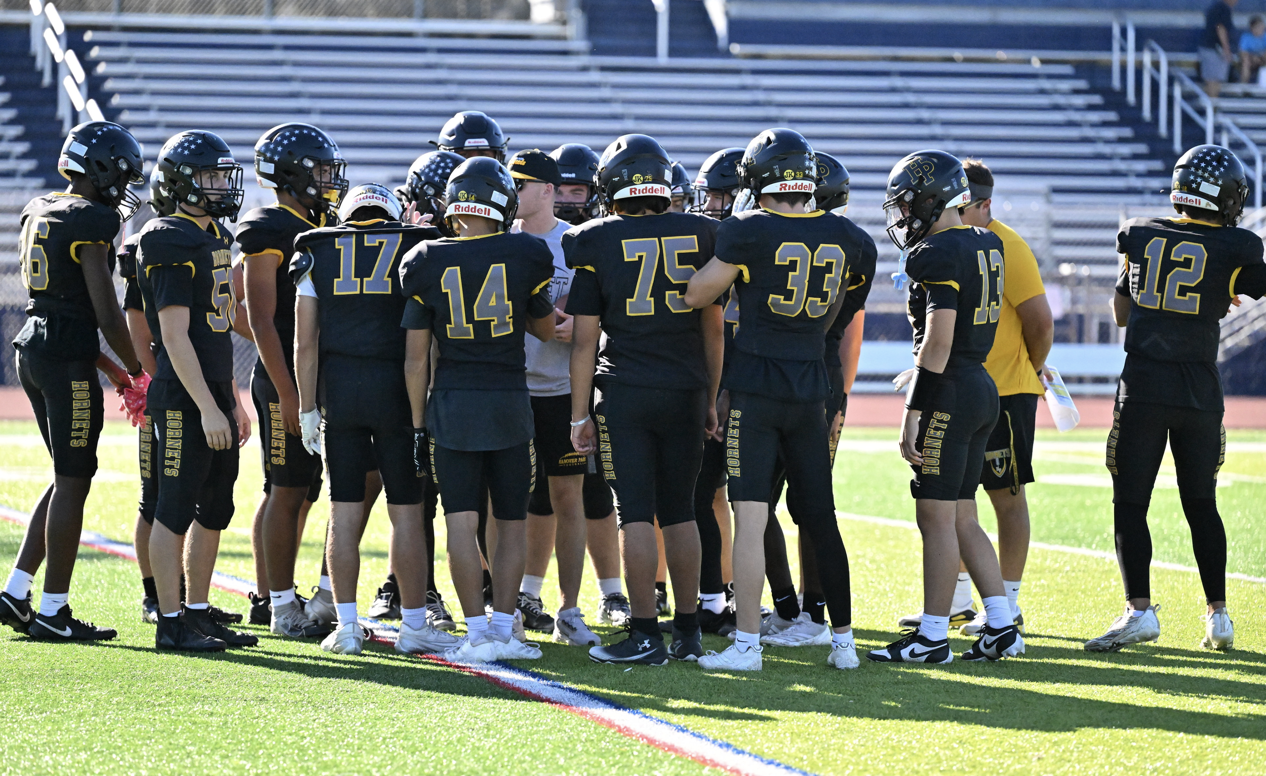 Youth football team in black uniforms gathered around coach on field during game.