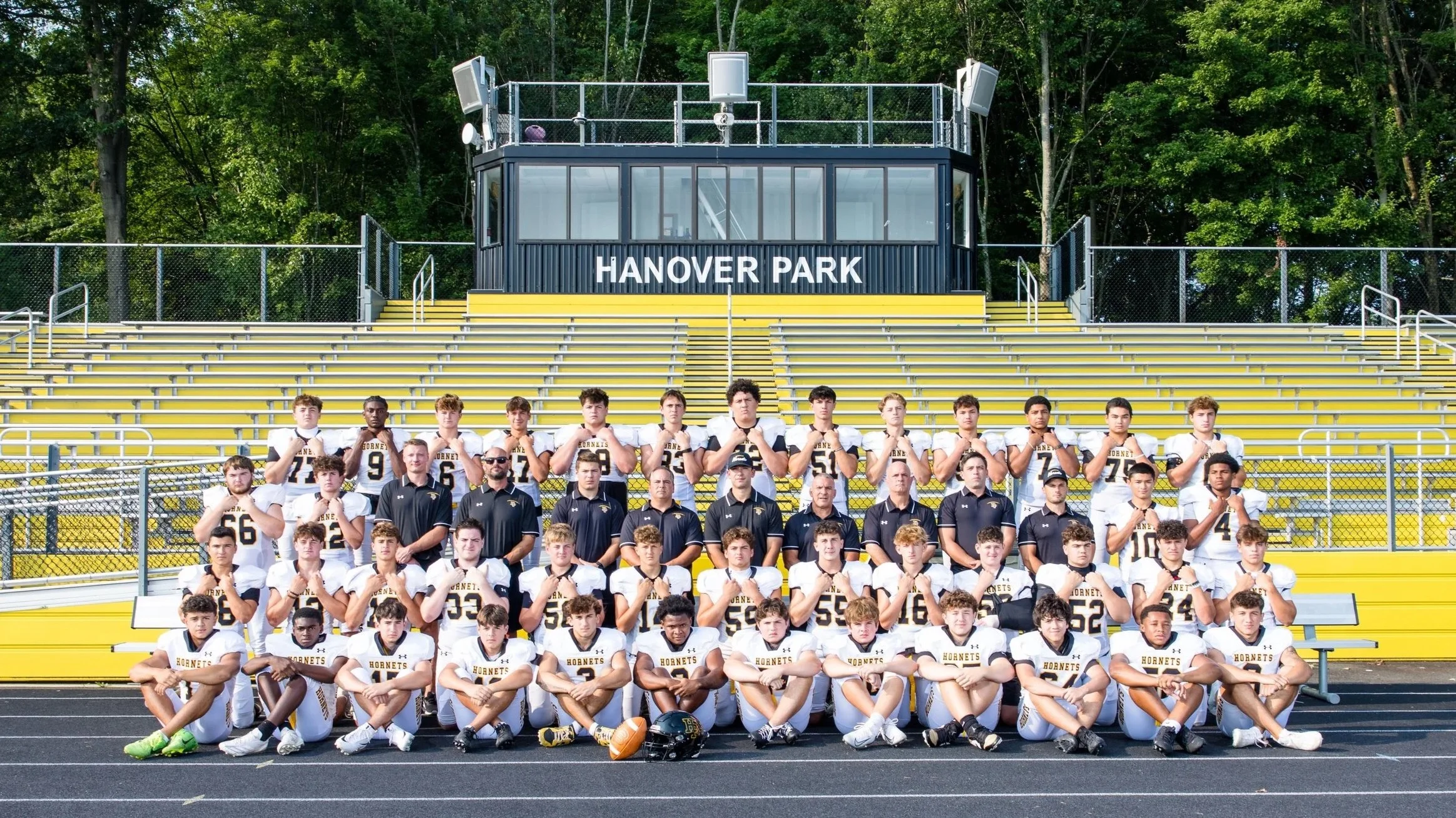 A group of football players and coaches posing for a team photo in front of bleachers at Hanover Park football stadium.