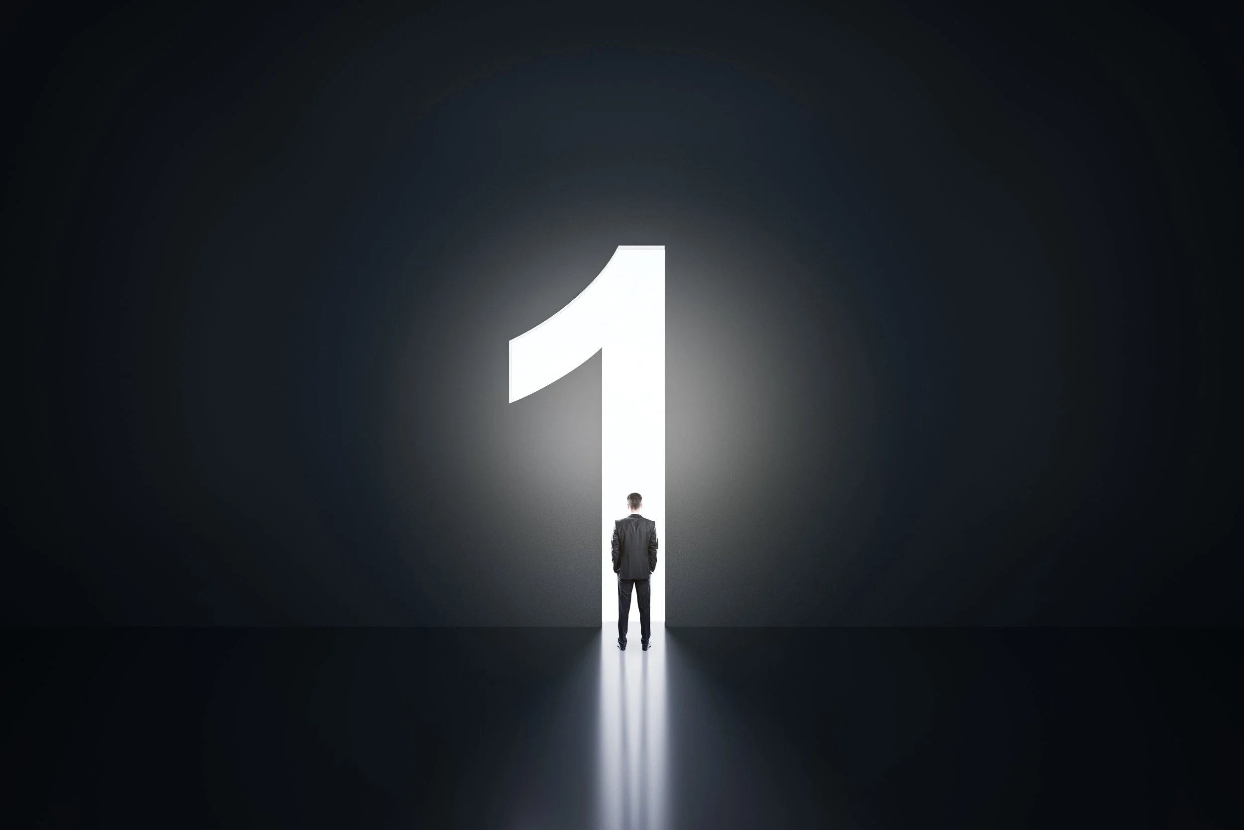 A businessman stands in front of a large illuminated number one, with a dark background creating a dramatic effect.