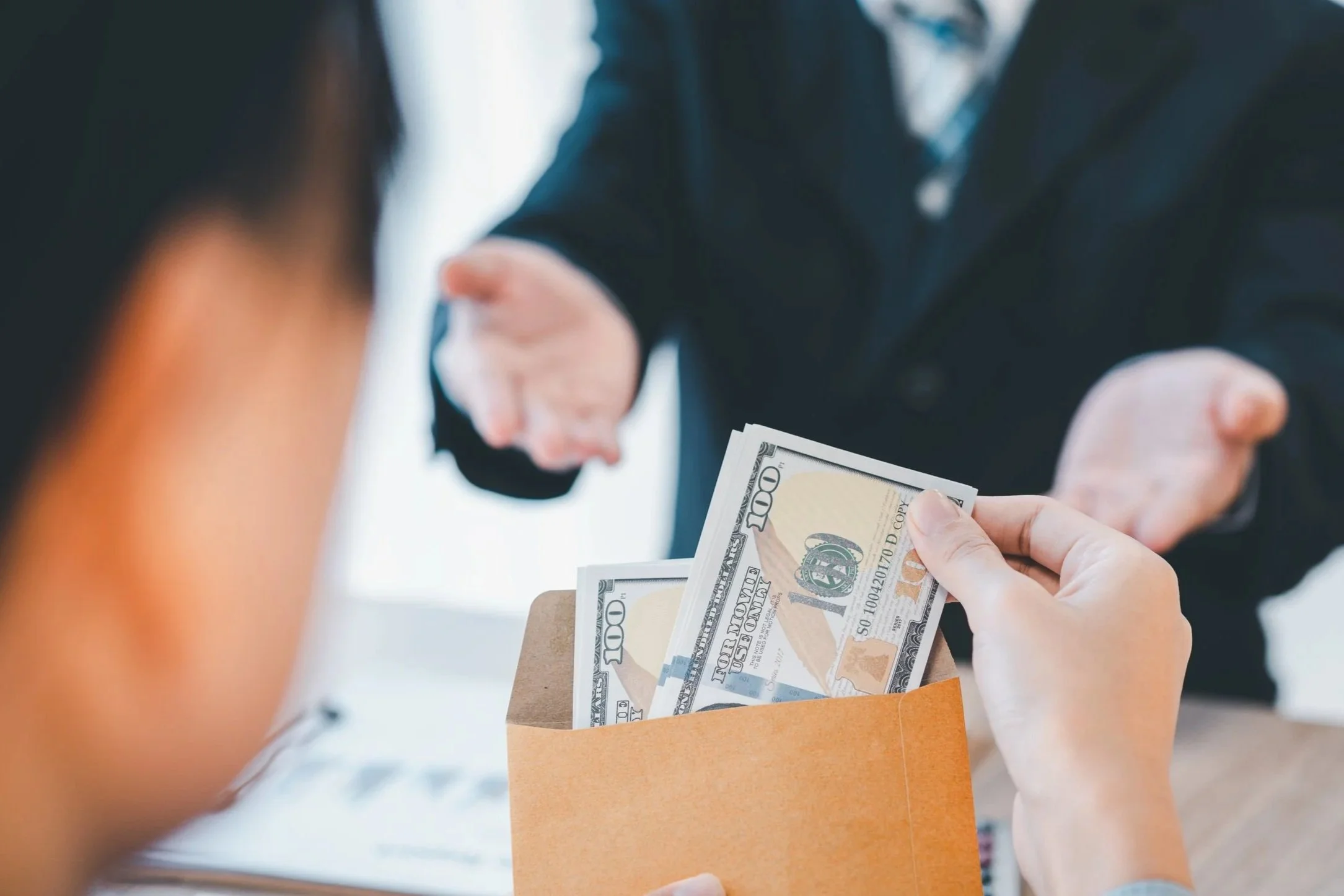Person handing over a stack of money to another person in a business setting.