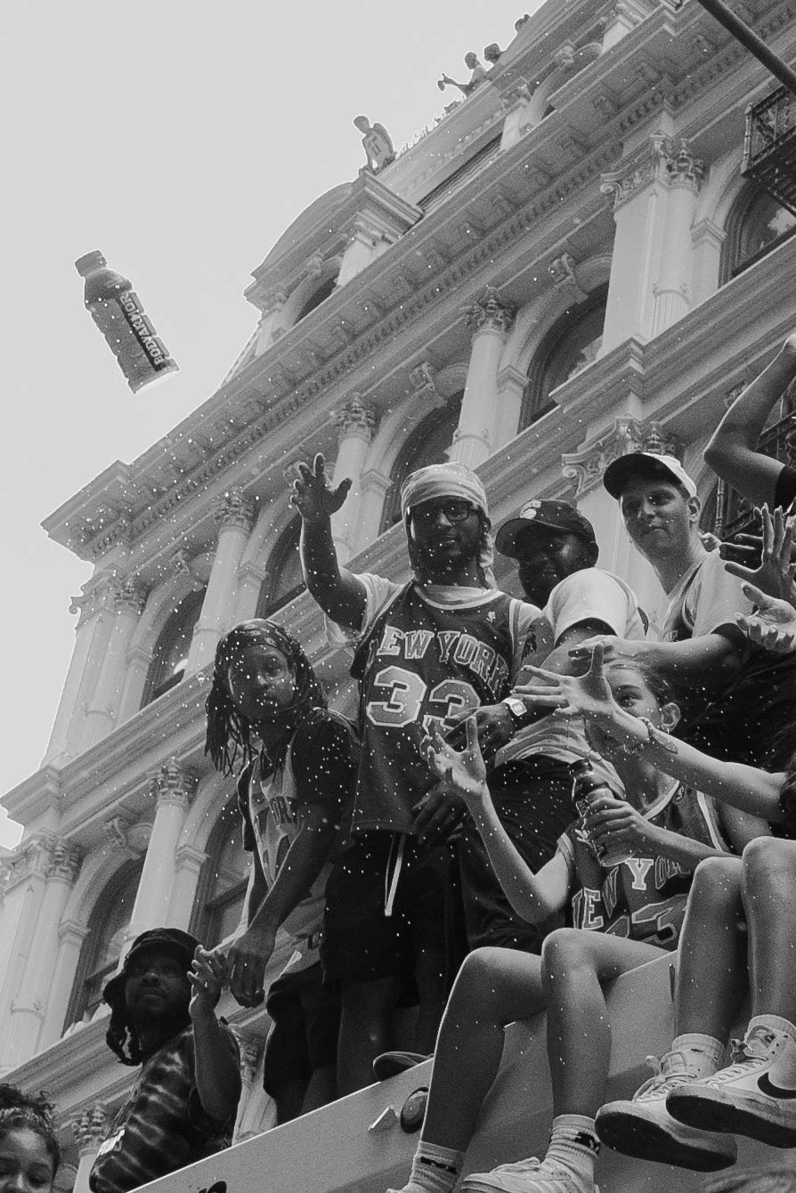 Group of people sitting on a float during a parade, with an ornate building in the background, engaging in a water spray celebration.
