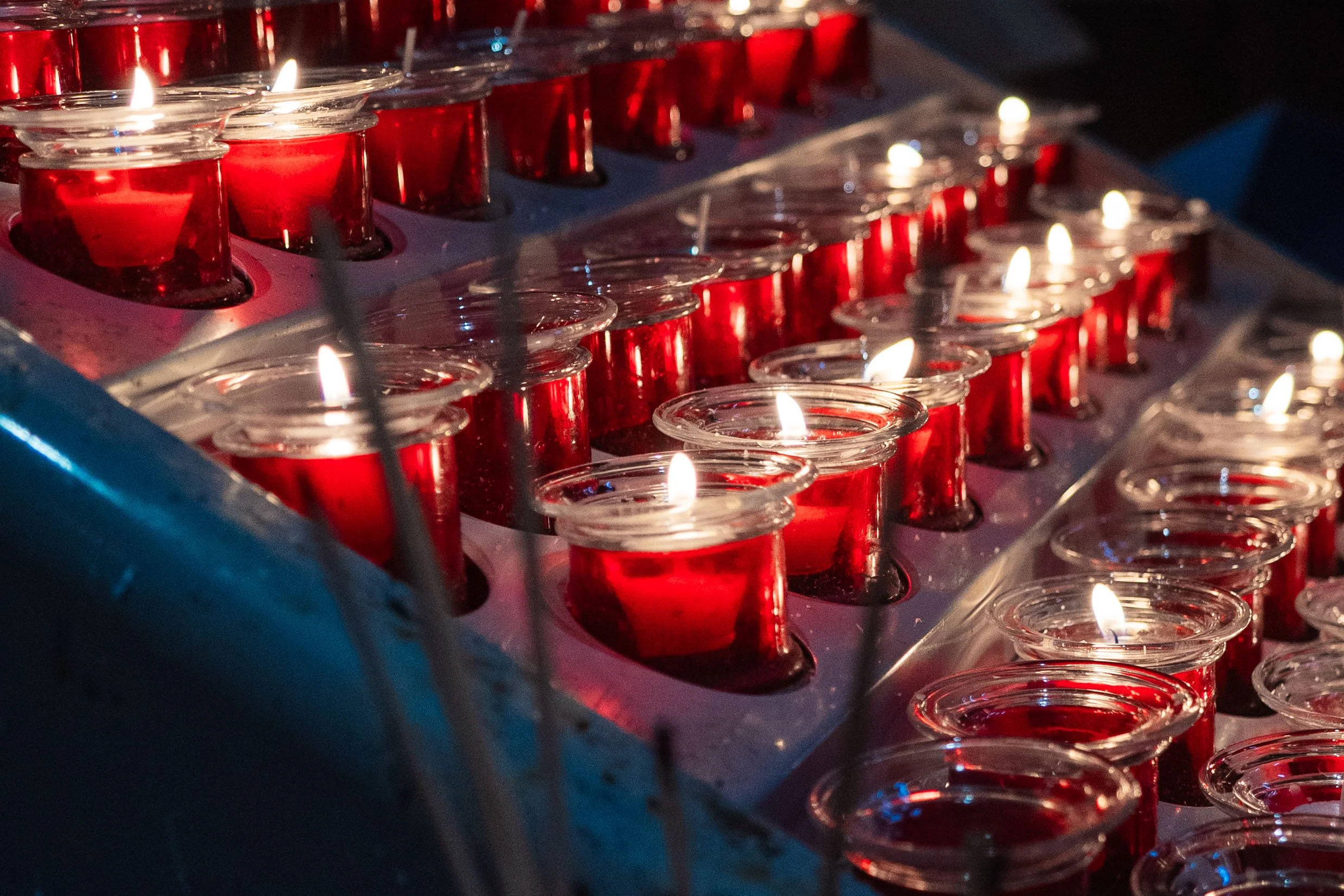 Multiple small red candles in glass holders arranged in rows