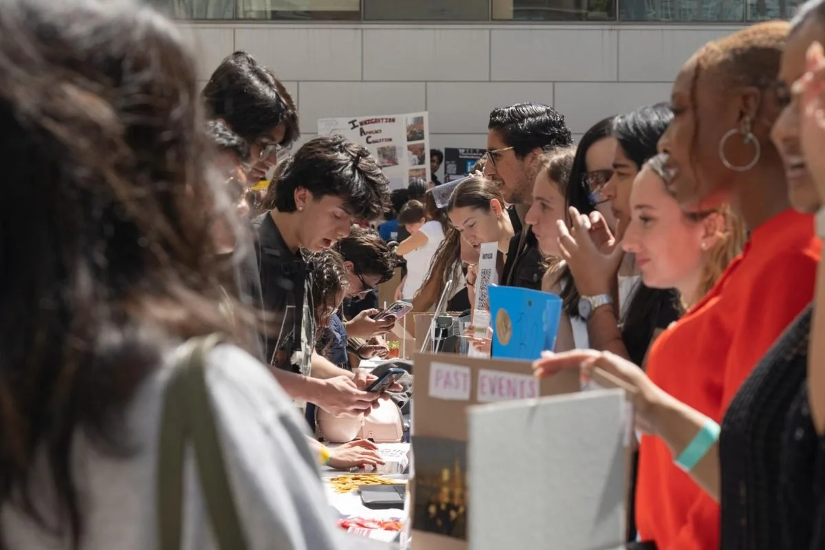 People gathered at a table, examining displays and using their phones at an event or exhibition.