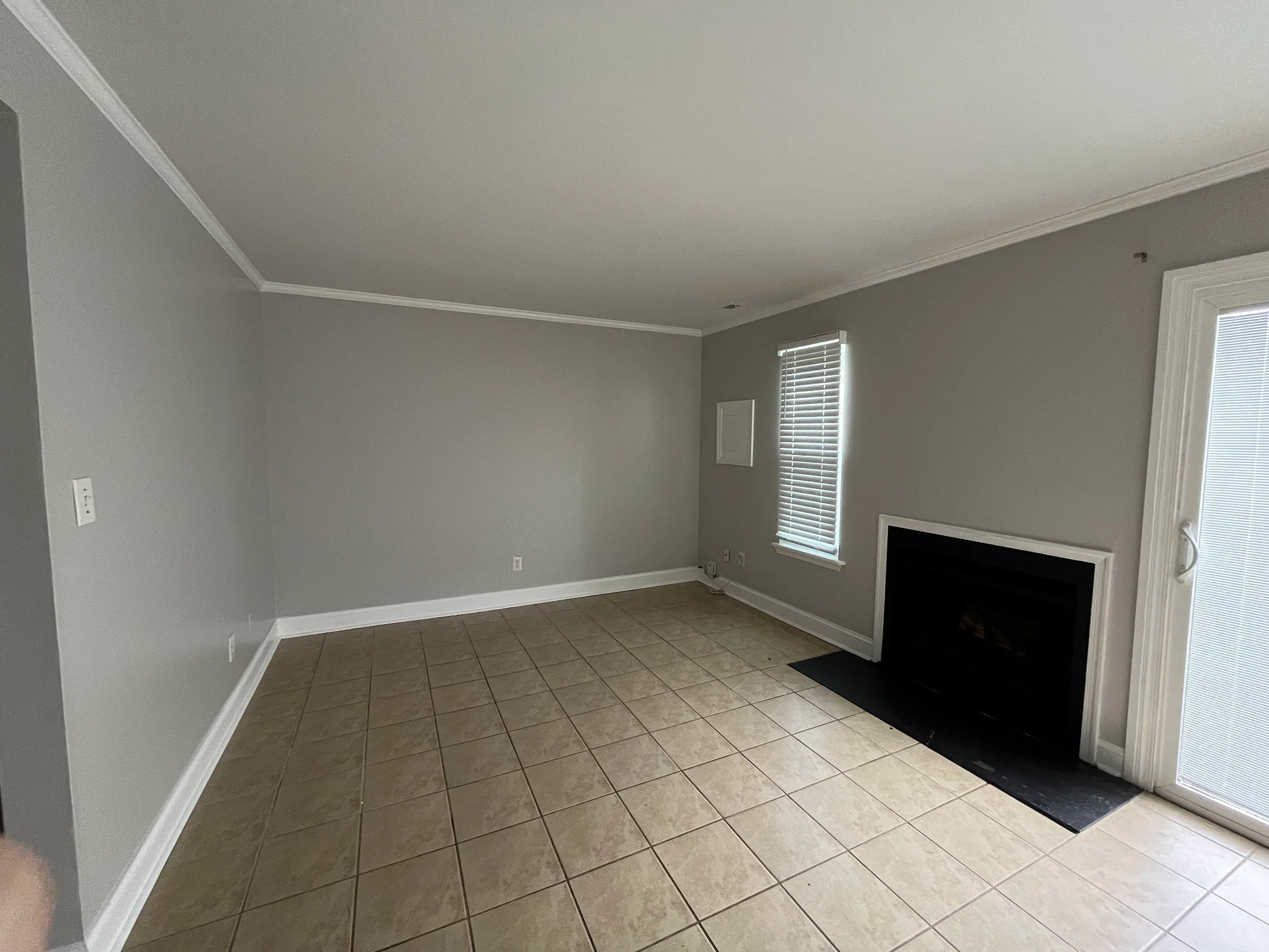Empty living room with tiled floor, gray walls, two windows with blinds, and a fireplace with a black hearth.