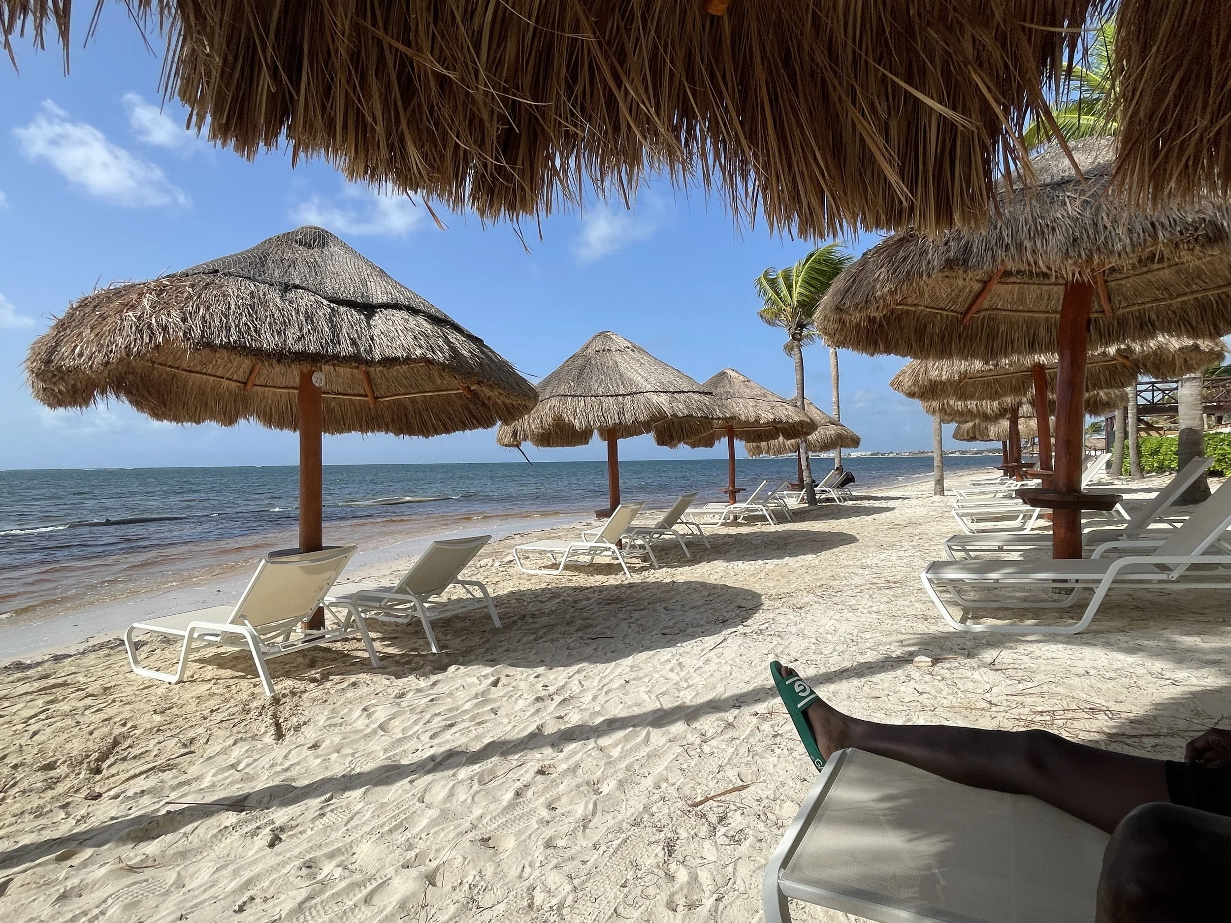 White-sand beach with shaded palapas and oceanfront lounge chairs at a luxury tropical resort.