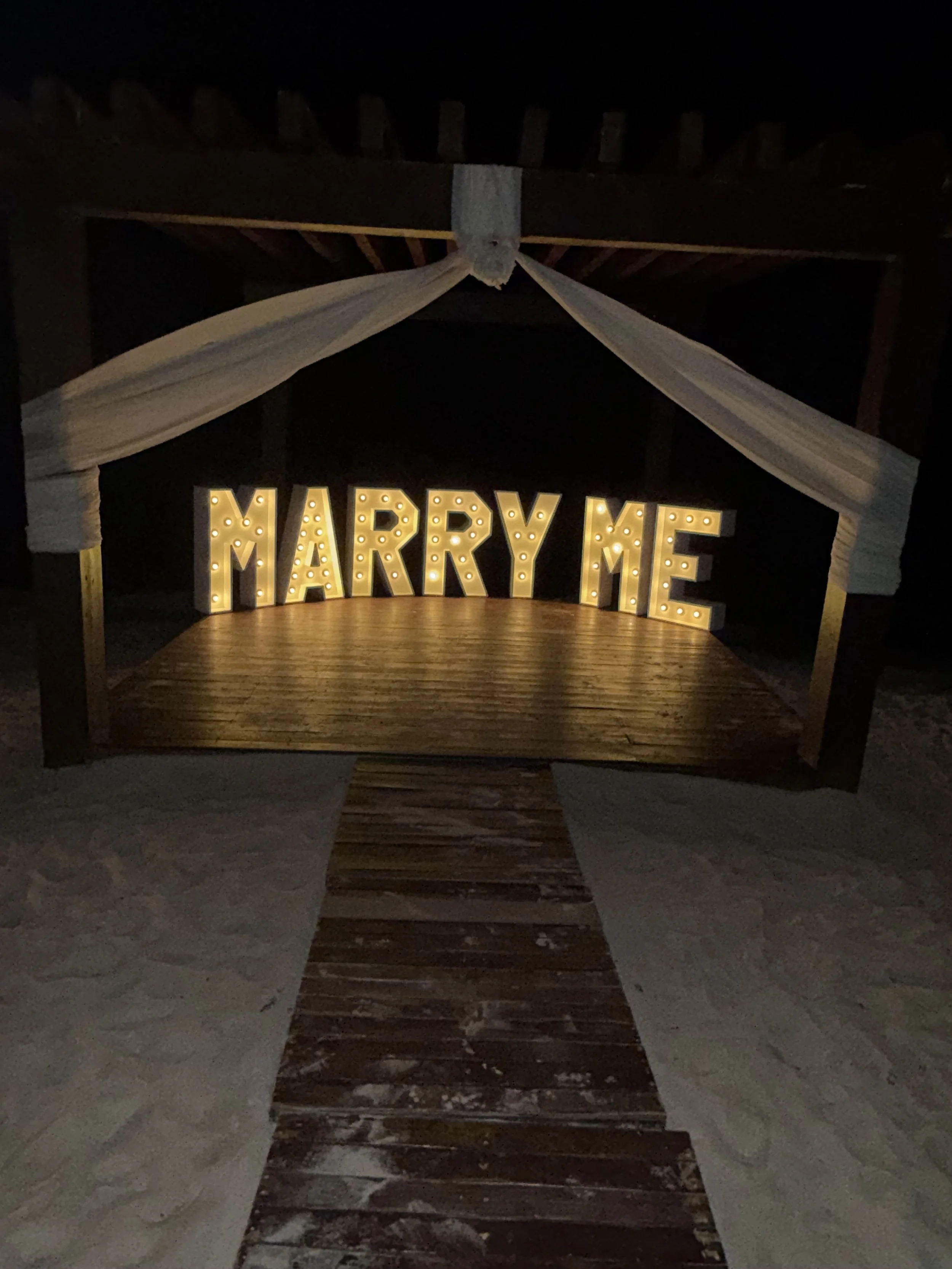 Romantic beachfront marriage proposal display illuminated with "Marry Me" lettering.