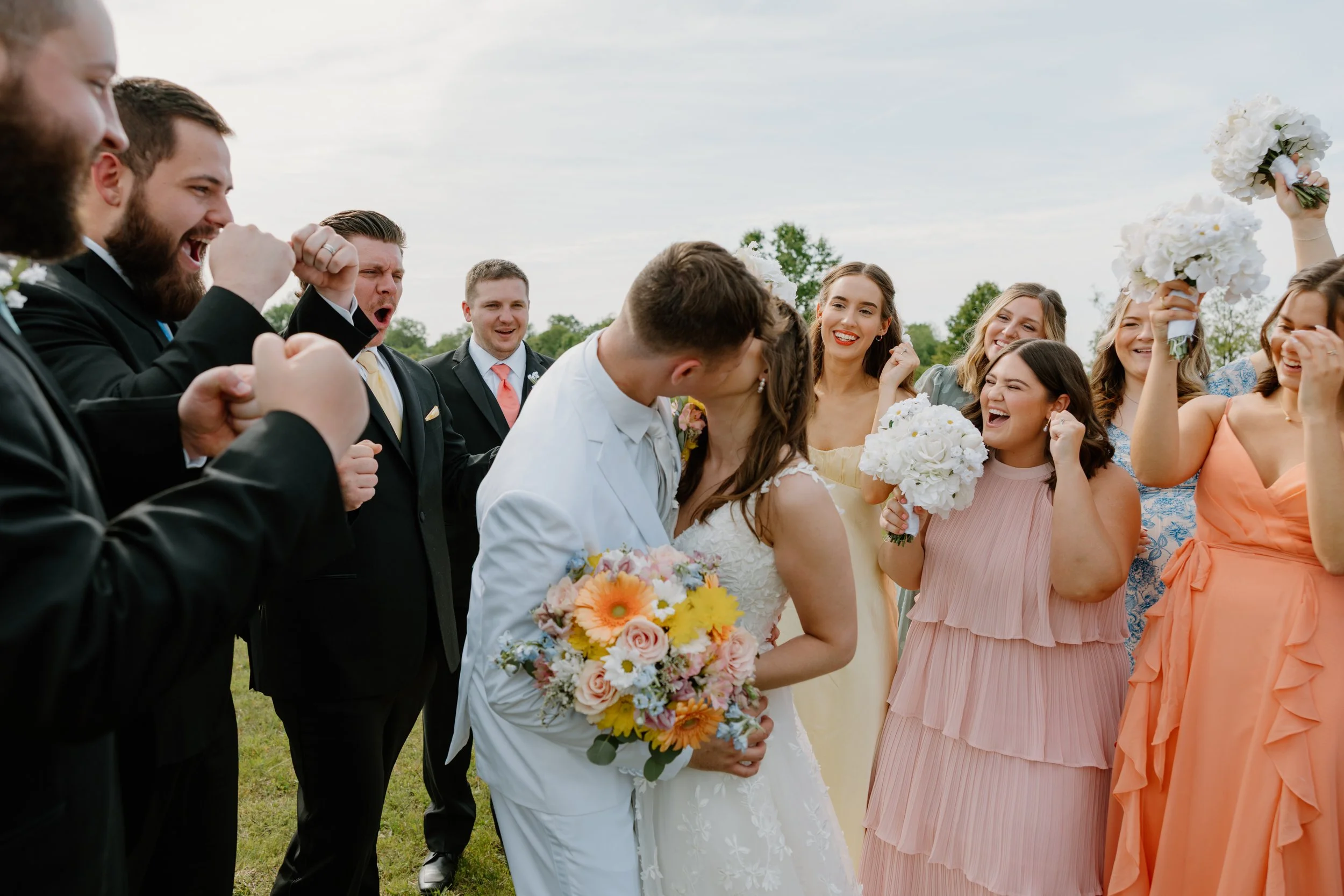 Group of wedding guests, including the bride and groom, celebrating outdoors with bouquets and joyful expressions.