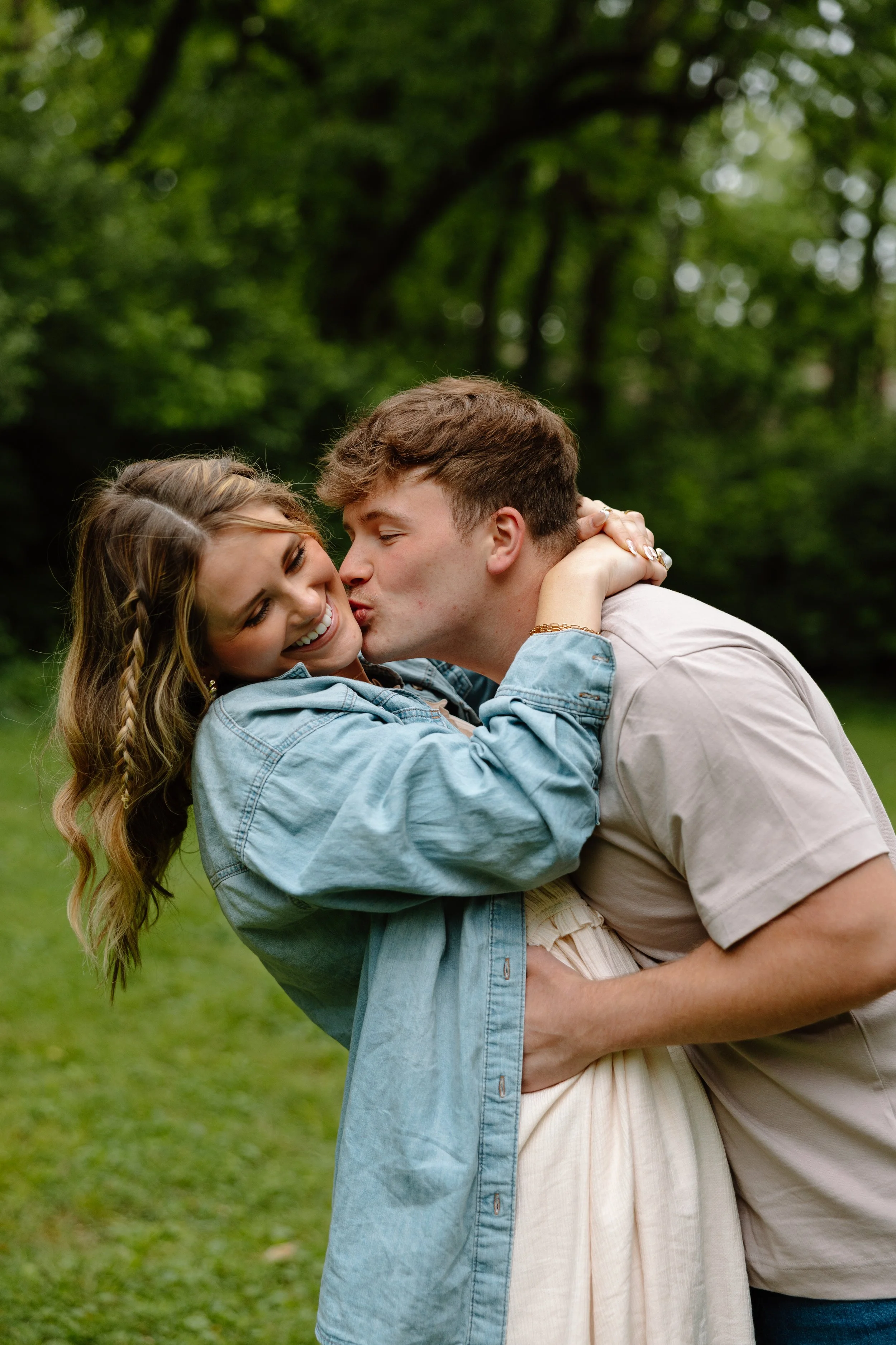 A young couple embracing outdoors in a park, with green trees in the background.