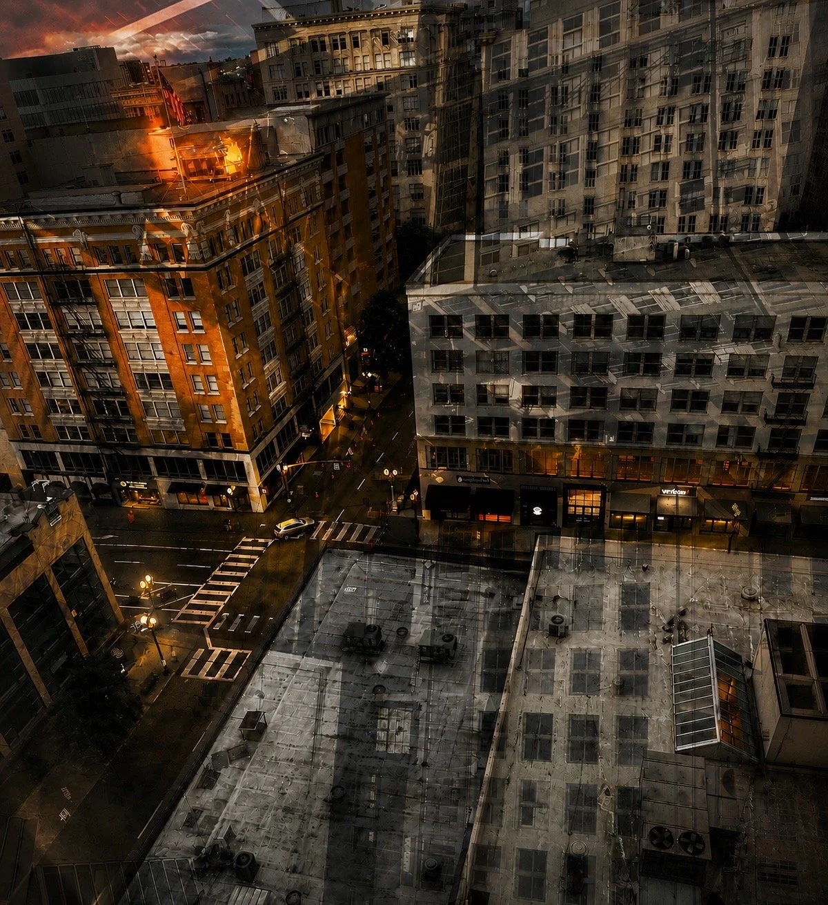 City view with tall buildings, streets, and reflections on a glass window, showing an urban neighborhood during dusk or dawn.