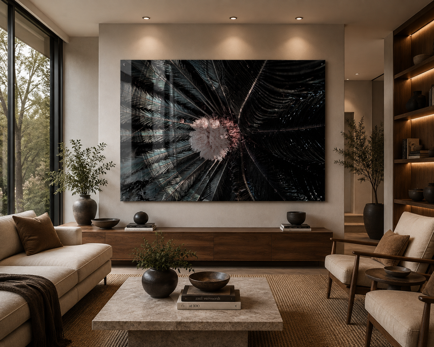 A modern living room with beige sofas, wooden coffee table, and large wall art depicting a close-up of palm leaves and a flower. The room has floor-to-ceiling windows with greenery outside, and decorative vases and books.