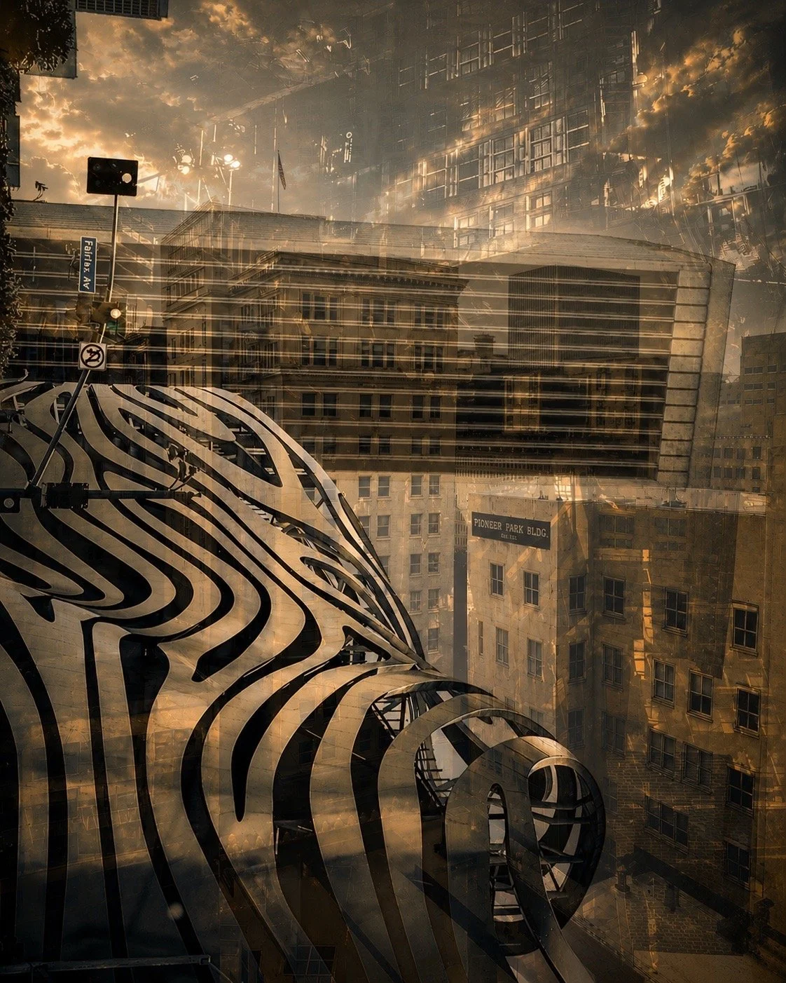 Architectural reflection photo showing a cityscape with a futuristic woven sculpture in the foreground, buildings, traffic signals, a street sign, and cloudy sky in the background.