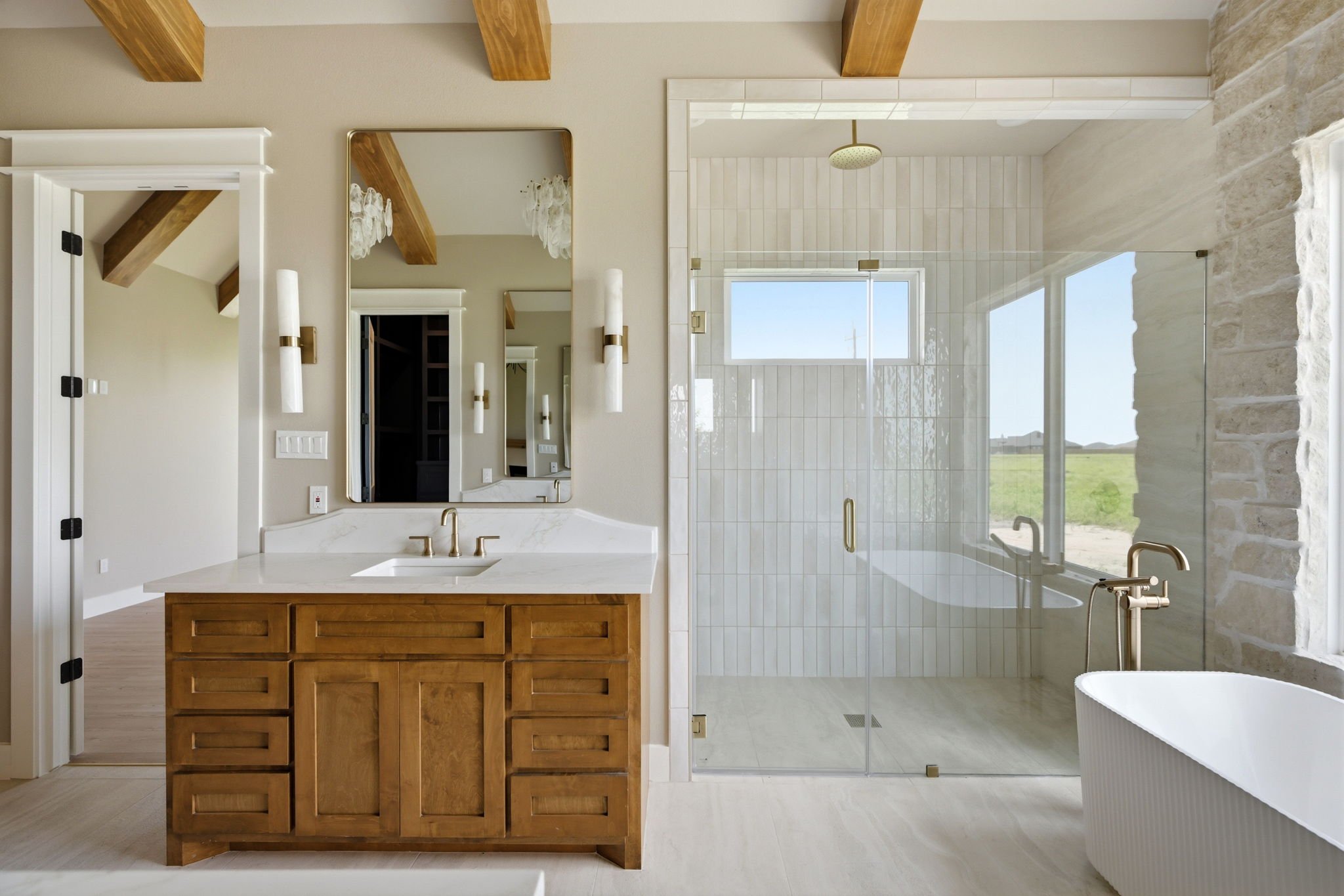 Modern bathroom with wooden vanity, large mirror, and glass shower enclosure with window, neutral color palette, and stone accents.