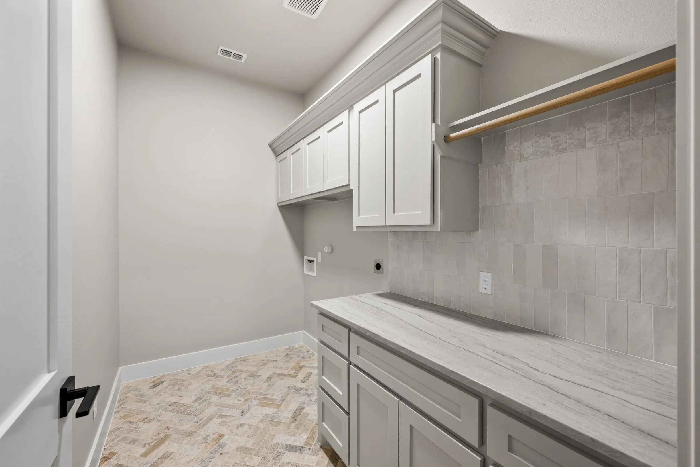 Empty laundry room with white cabinets, marble countertop, beige tile backsplash, and a linen closet with a wooden rod for hanging clothes.