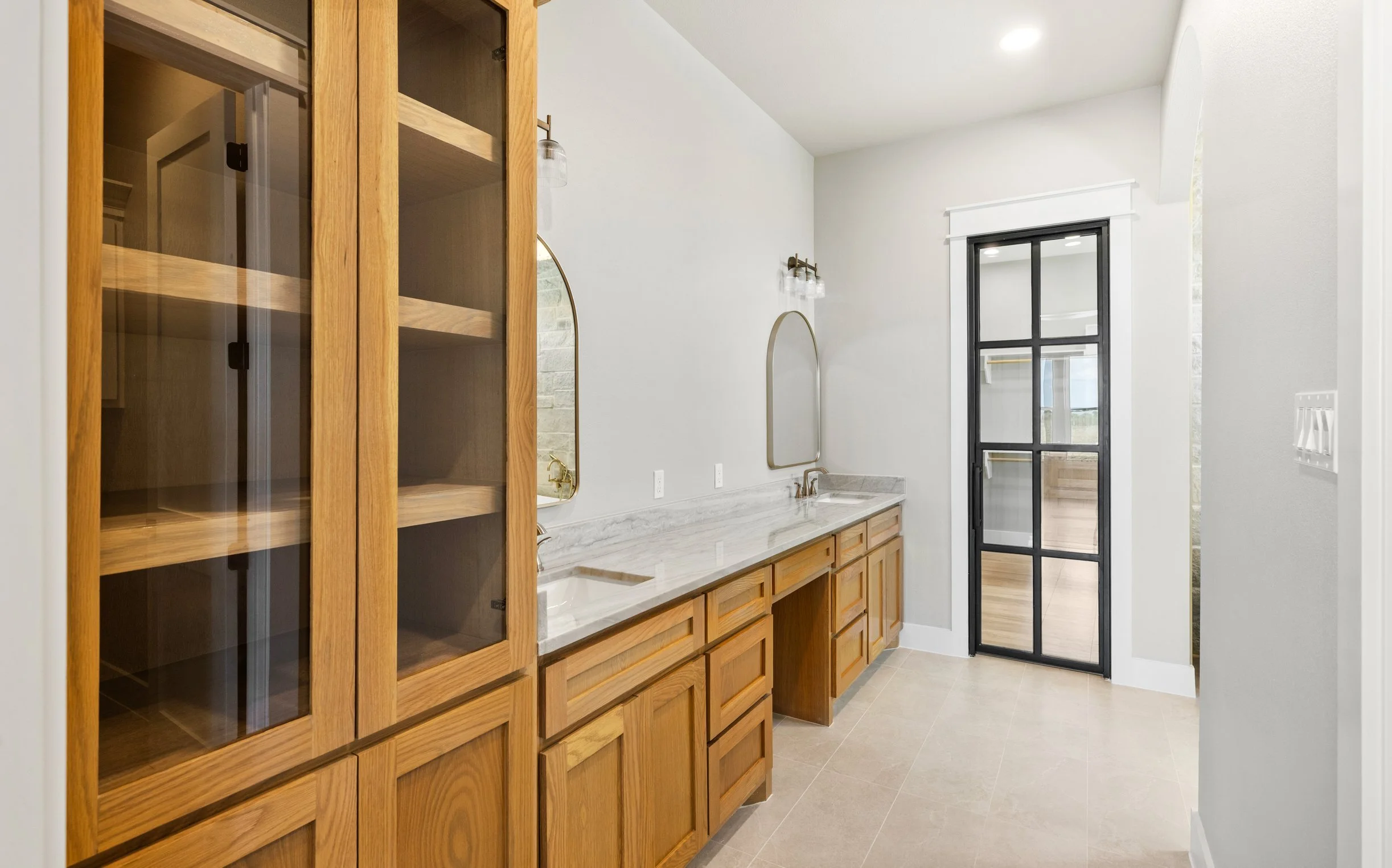 Bathroom with wooden cabinets, marble countertop, and a black-framed glass door.