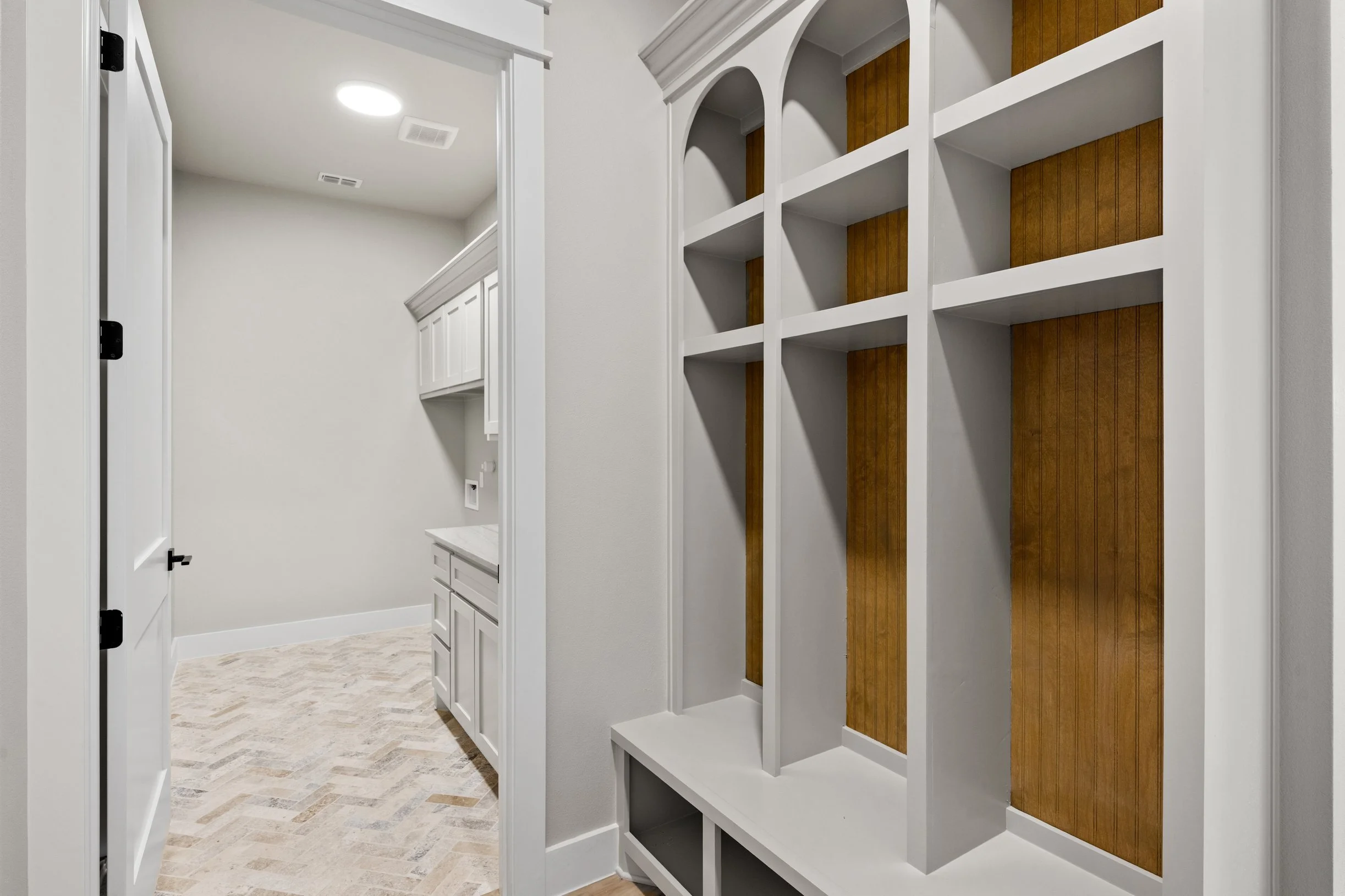 A view inside a home, showing built-in white shelves with brown paneling, and part of a laundry or utility room with white cabinetry and a marble countertop, all with a light-colored wood floor.