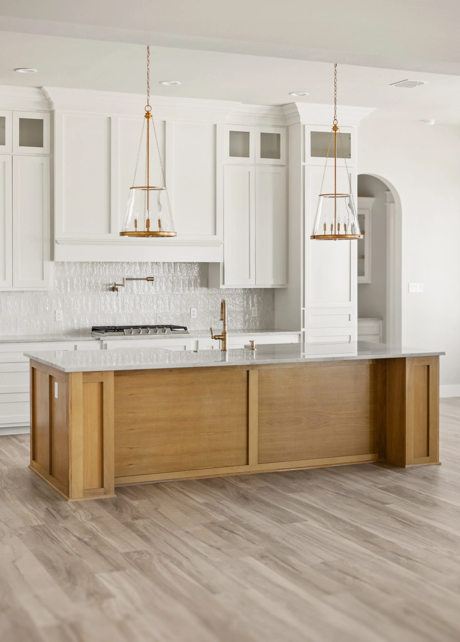 Modern kitchen with white cabinetry, a white countertop island with wooden sides, brass light fixtures, and light wood flooring.
