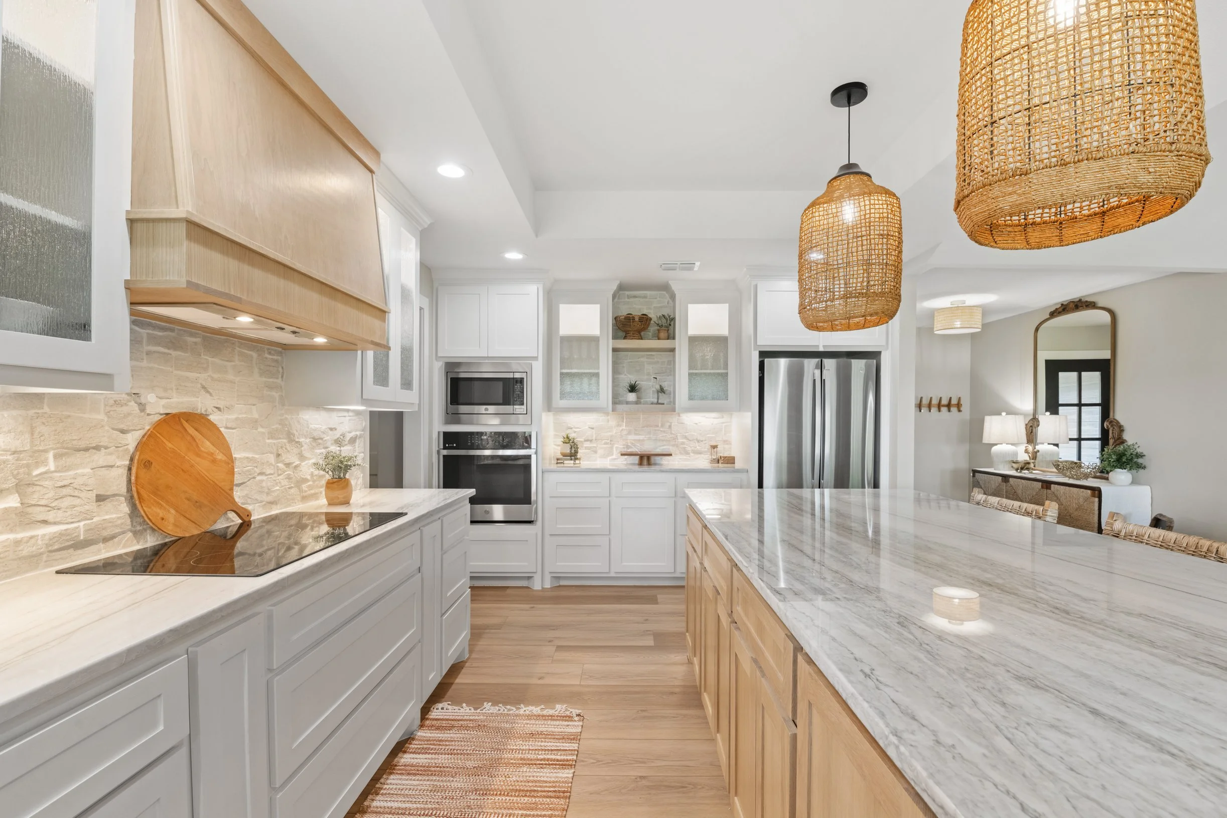 Modern kitchen with white cabinetry, stone accents, and a large marble island, featuring woven pendant lights hanging from the ceiling.