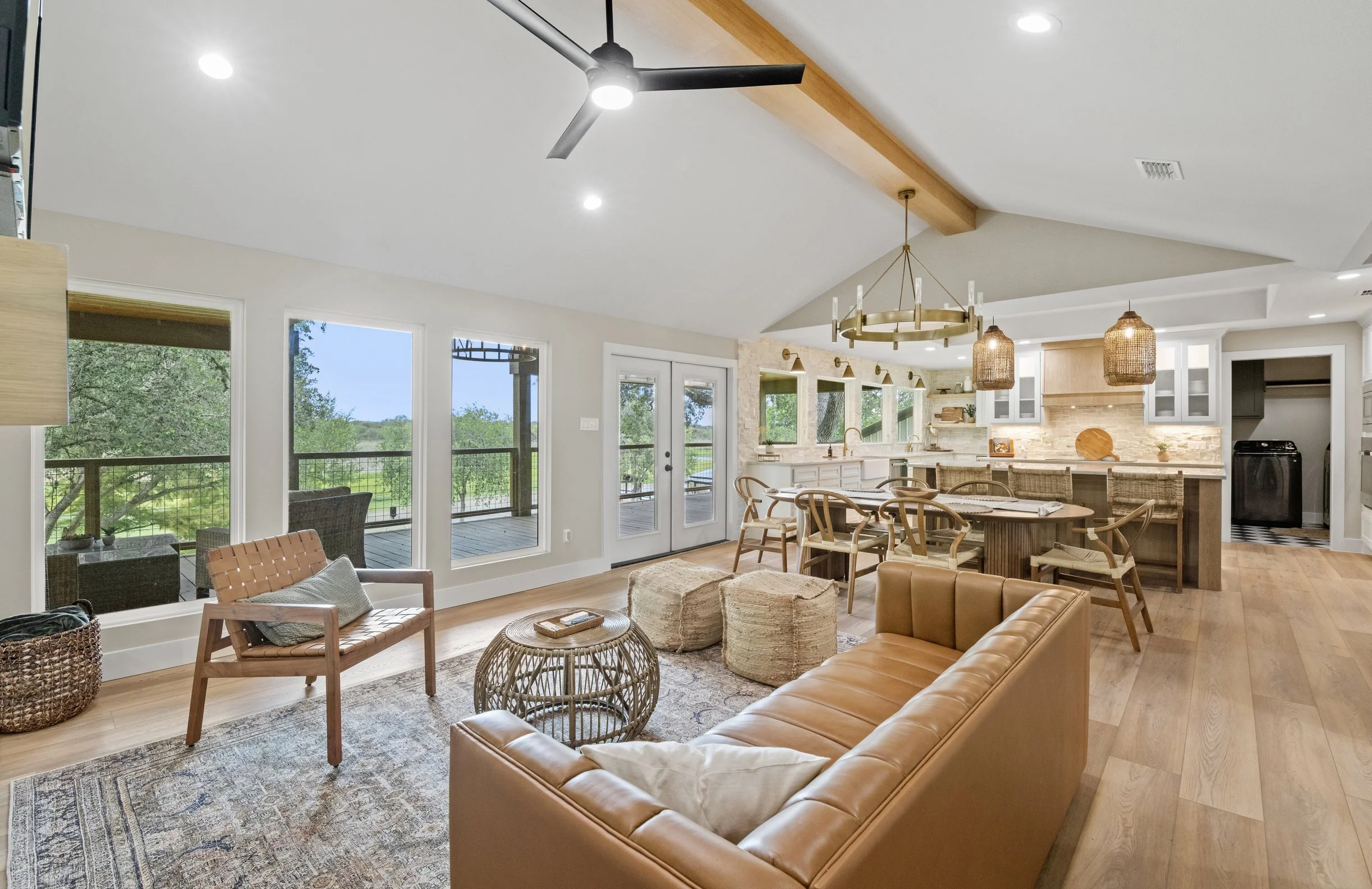 Open-concept living room and kitchen with large windows, wooden accents, a ceiling fan, and modern decor.