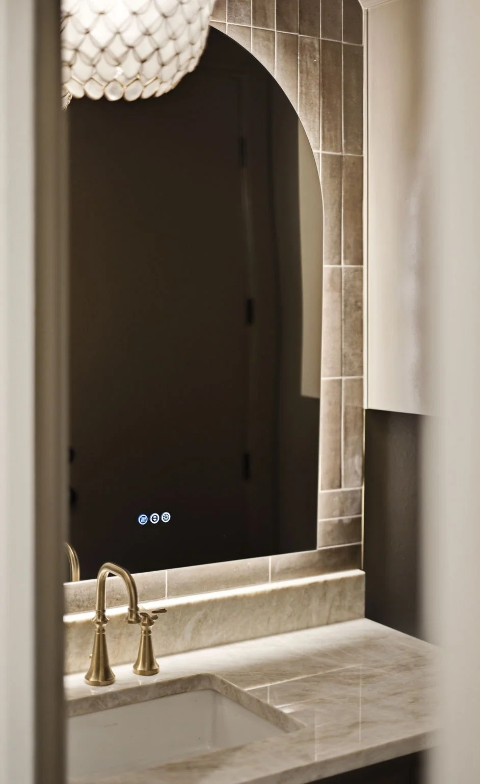 Bathroom with marble countertop, gold faucet, mirror, and tiled wall.