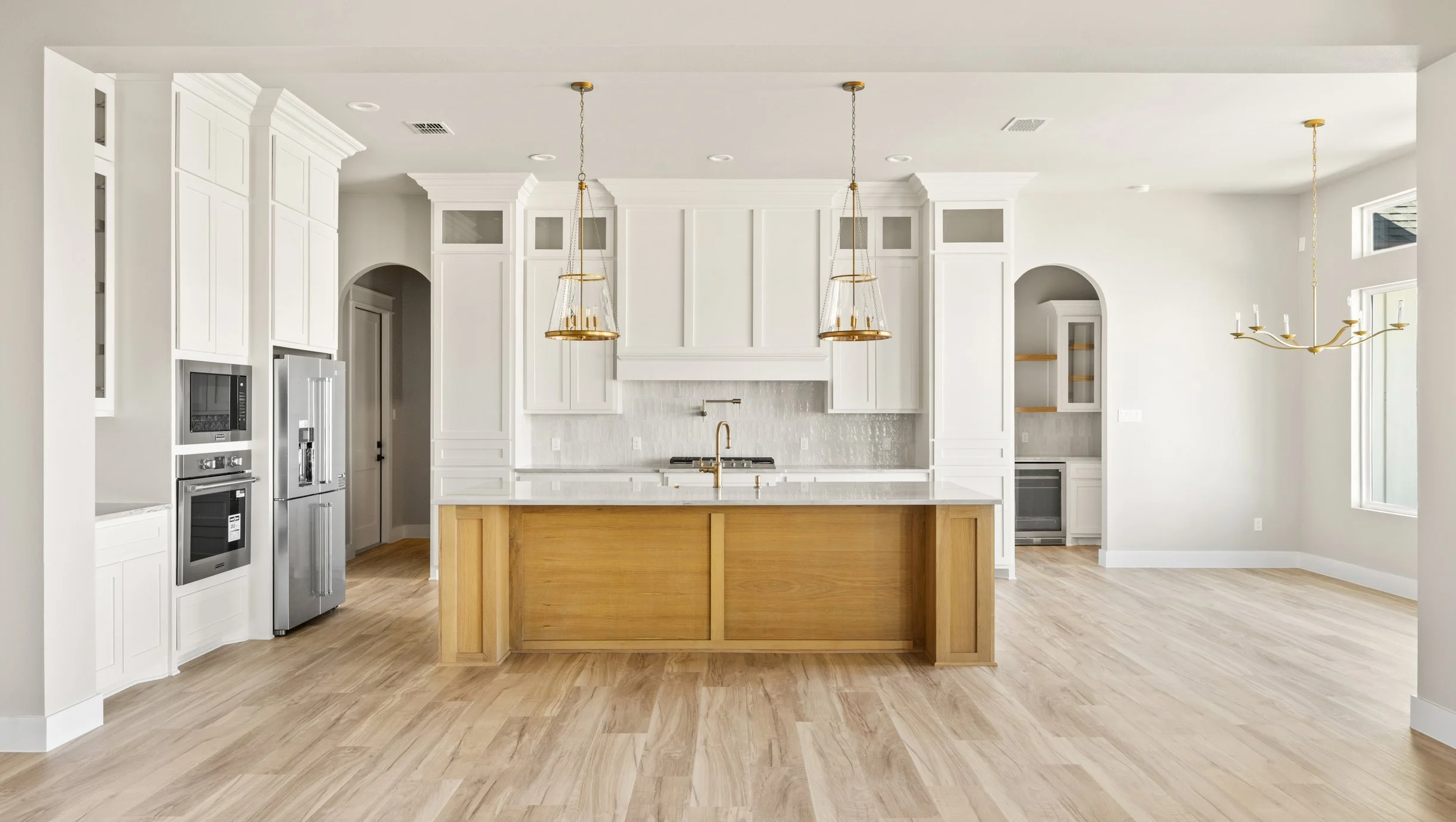 Modern white kitchen with a large wooden island, built-in appliances, pendant lighting, and a chandelier.