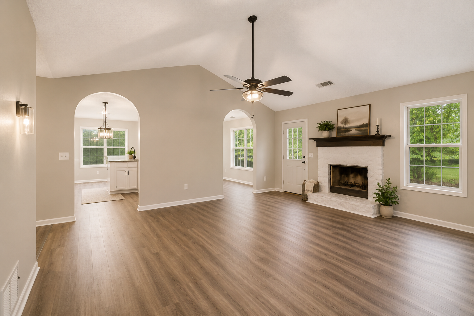Empty living room with wood floors, fireplace, ceiling fan, large windows, doorway, and view into dining area with hanging light fixture. Completed by Sawdust.