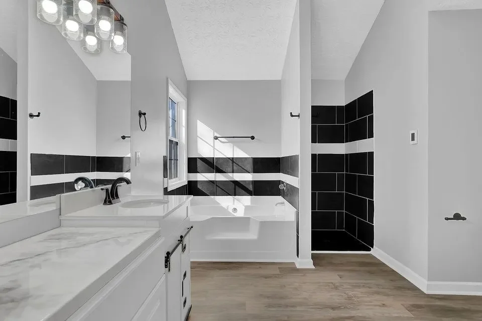 Modern bathroom with a white vanity, marble countertop, and black fixtures, a bathtub with a window, and a separate black-tiled shower stall. Completed by Sawdust.