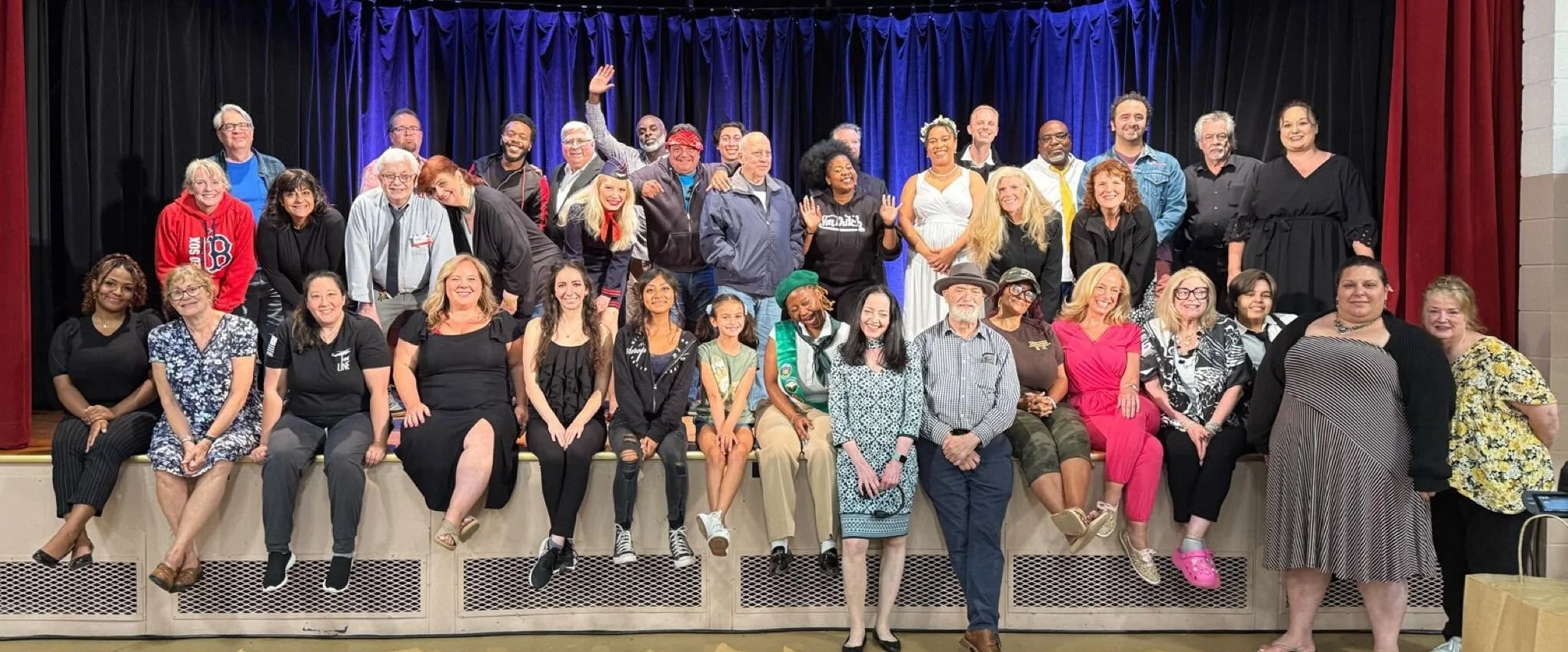 A large group of diverse people posing on a stage with dark blue curtains in the background.