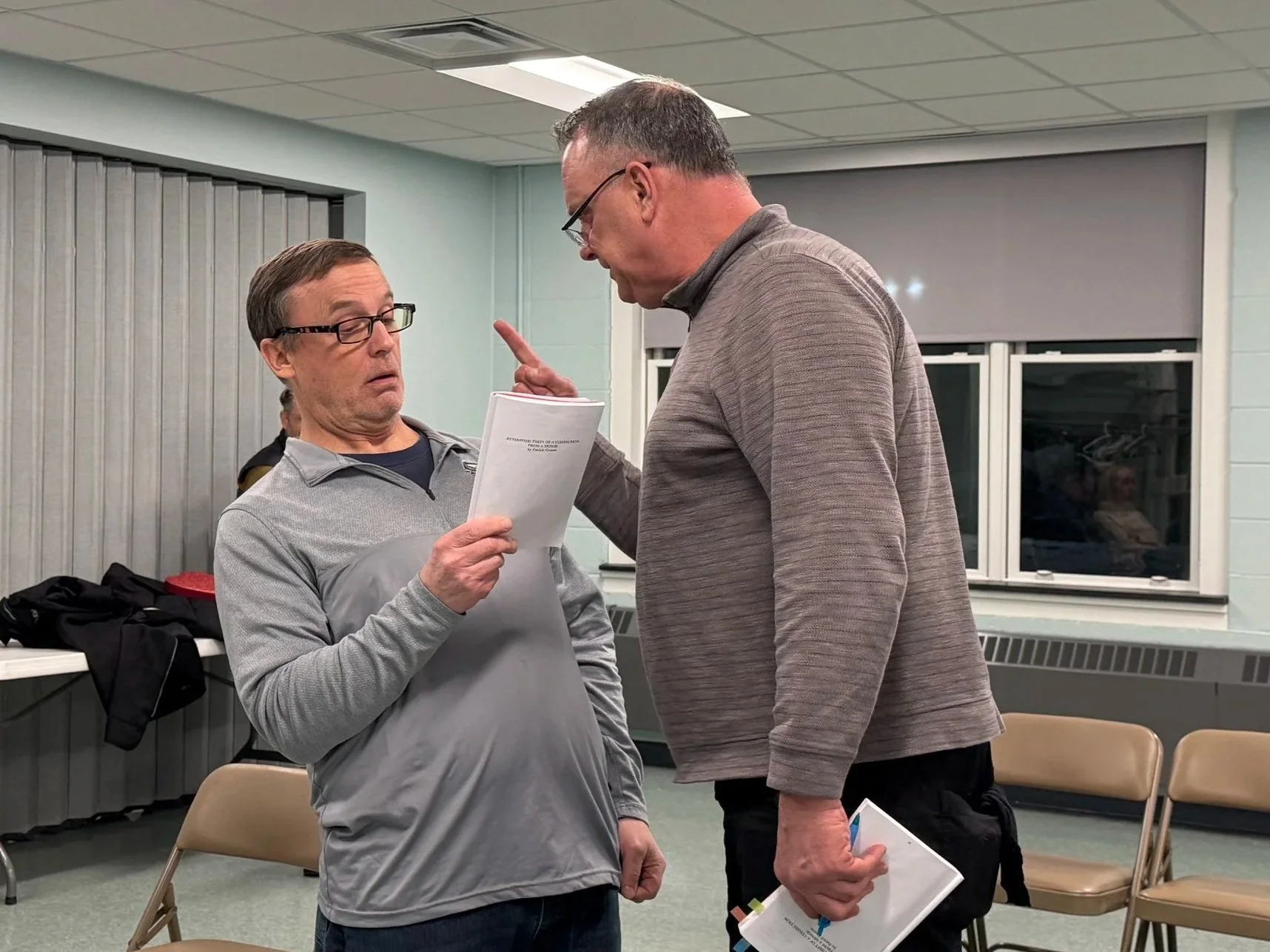 Two men in conversation at a meeting room, with one man appearing surprised and the other gesturing with his finger.