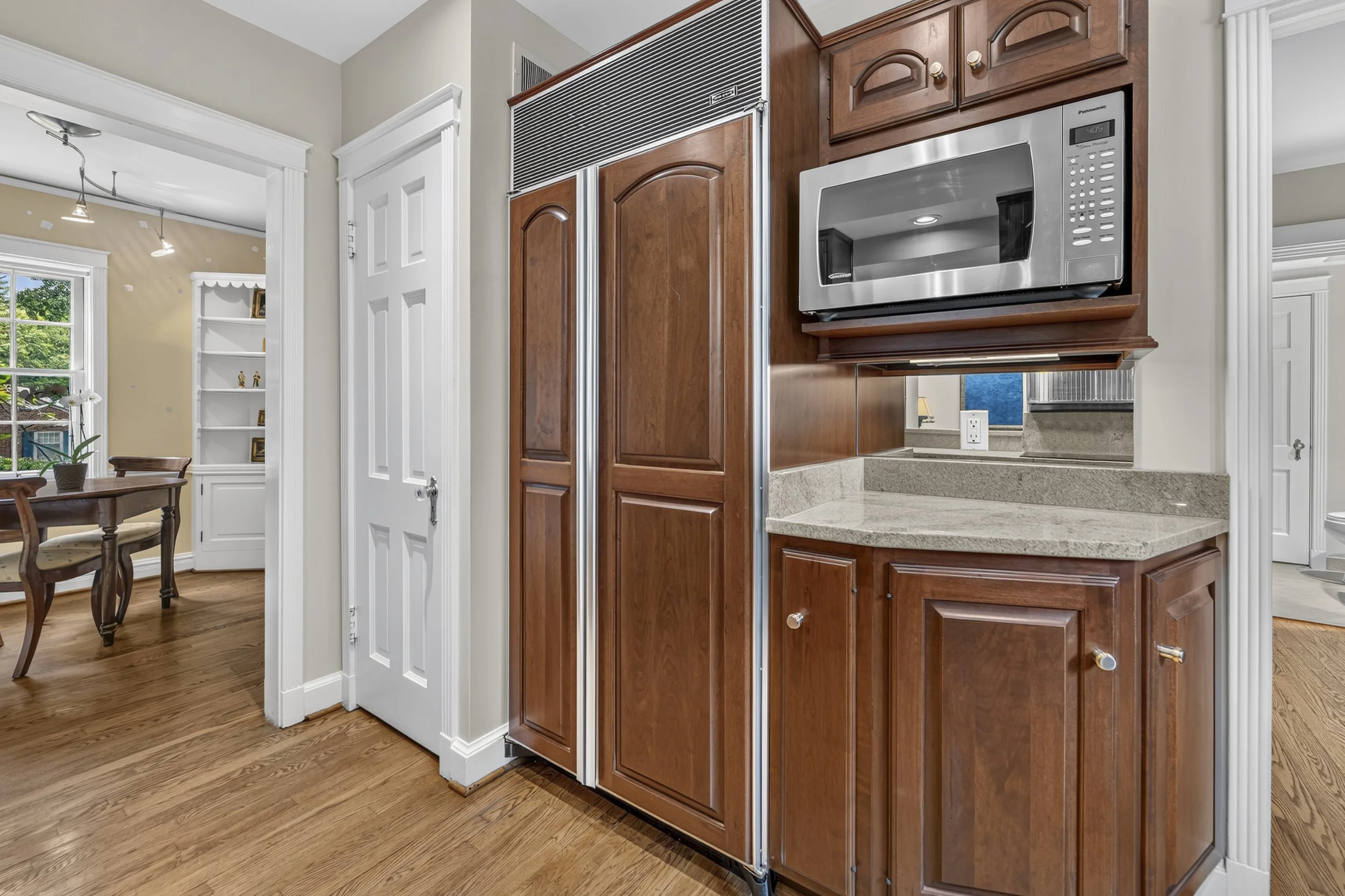 View of a kitchen with wooden cabinets, a microwave, and a granite countertop, with a living room area visible in the background.