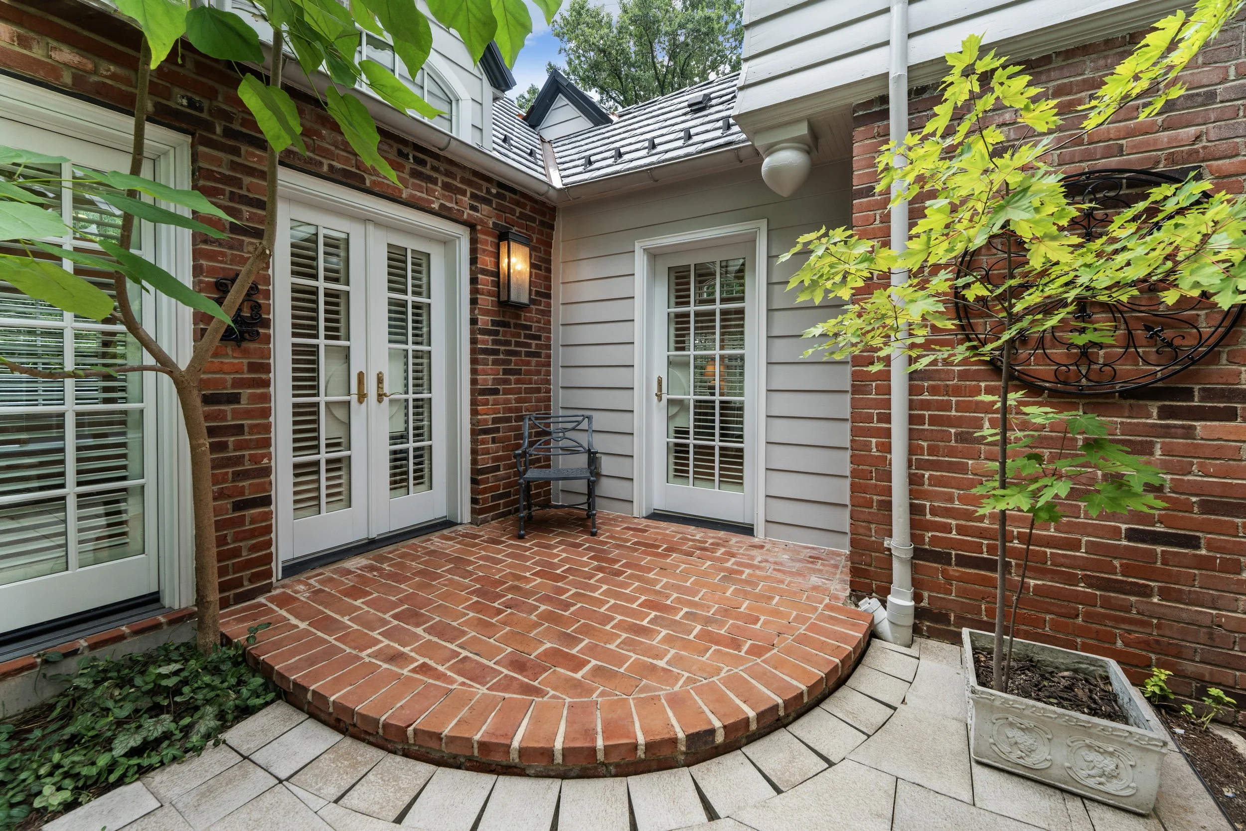 Brick rear patio featuring French doors, outdoor lighting, and landscaped surroundings.