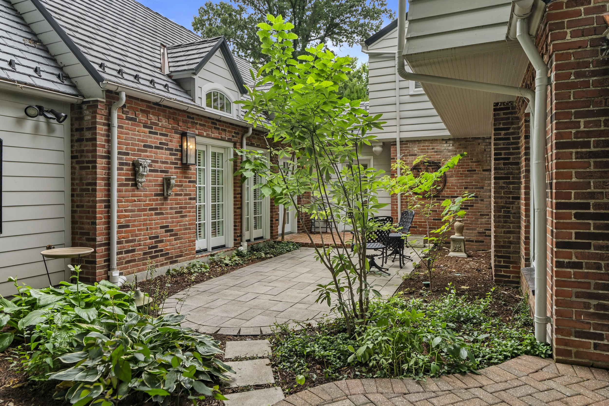 Private brick patio with landscaped gardens and covered outdoor living space.