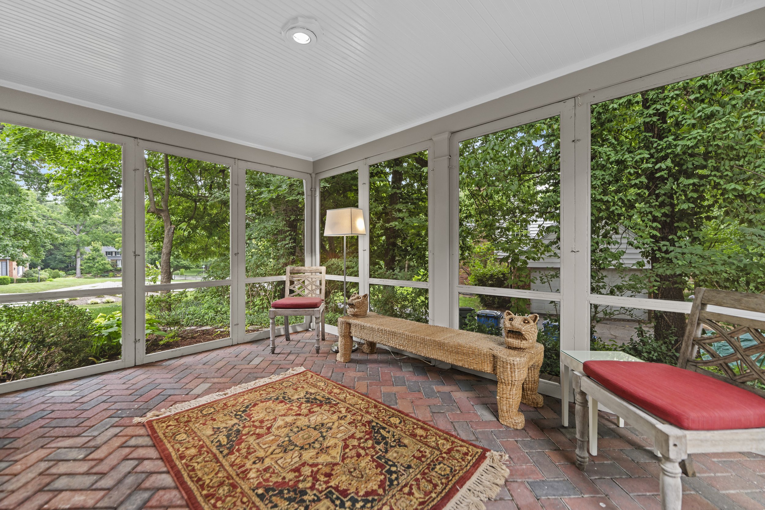 Screened porch with comfortable seating, brick flooring, and peaceful views of the landscaped grounds.