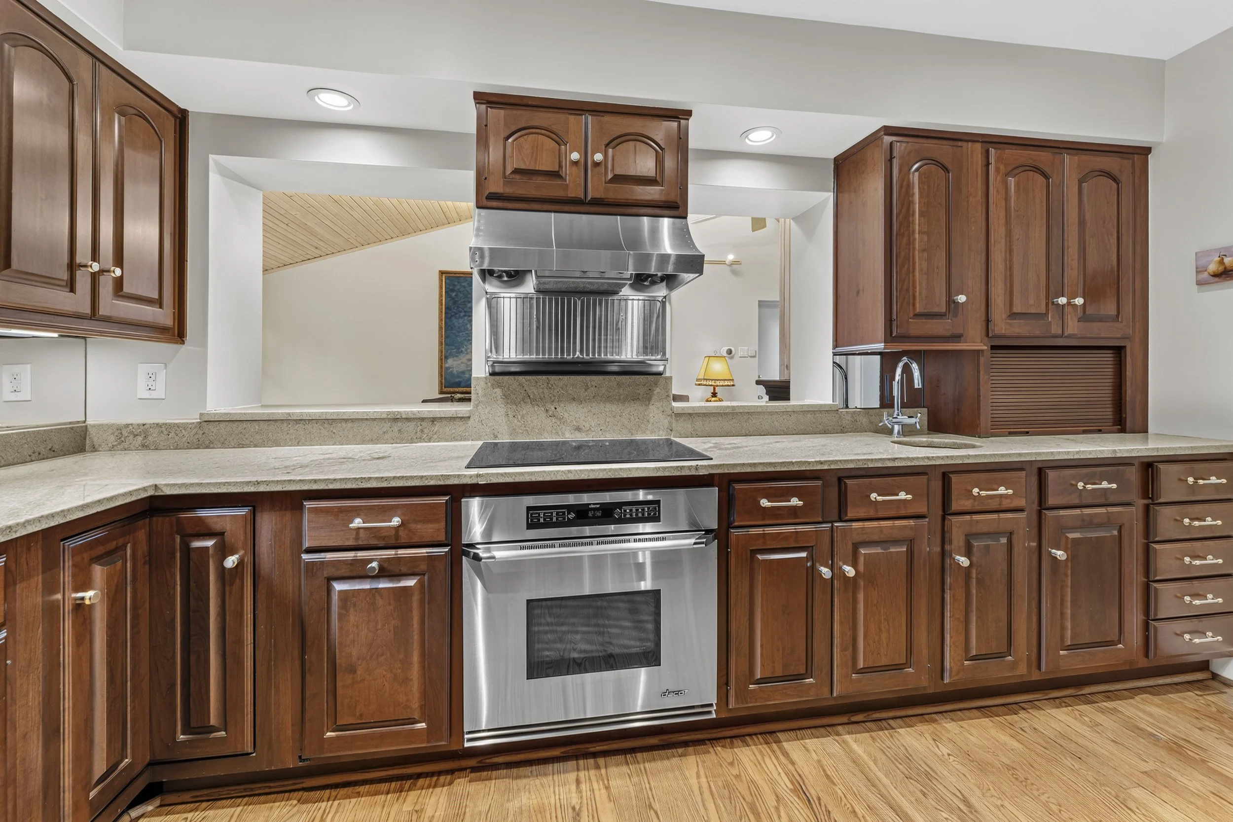 Kitchen with wooden cabinets, stainless steel dishwasher, granite countertops, and hardwood floors.