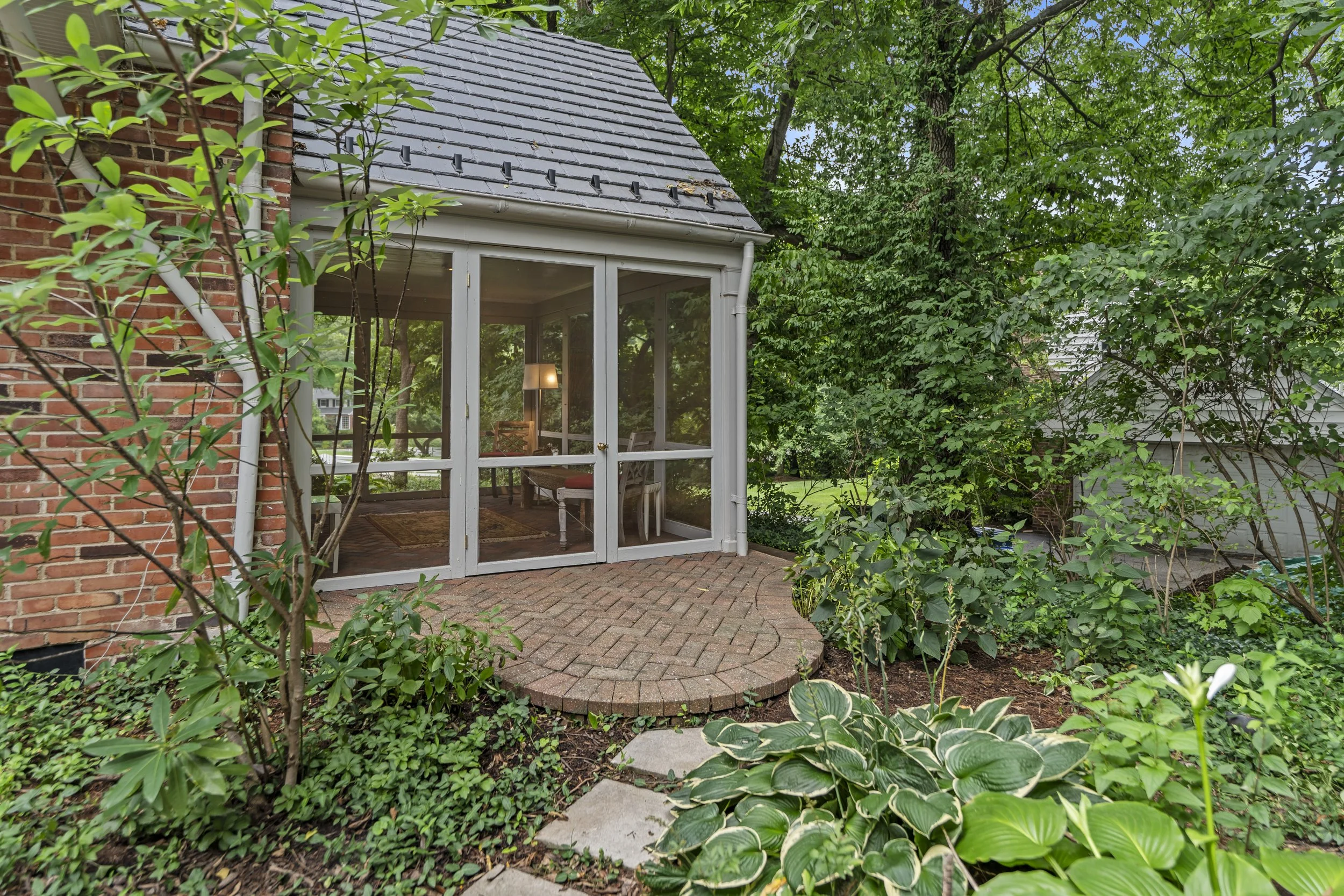 Screened porch overlooking mature landscaping and connecting to the brick patio and backyard.