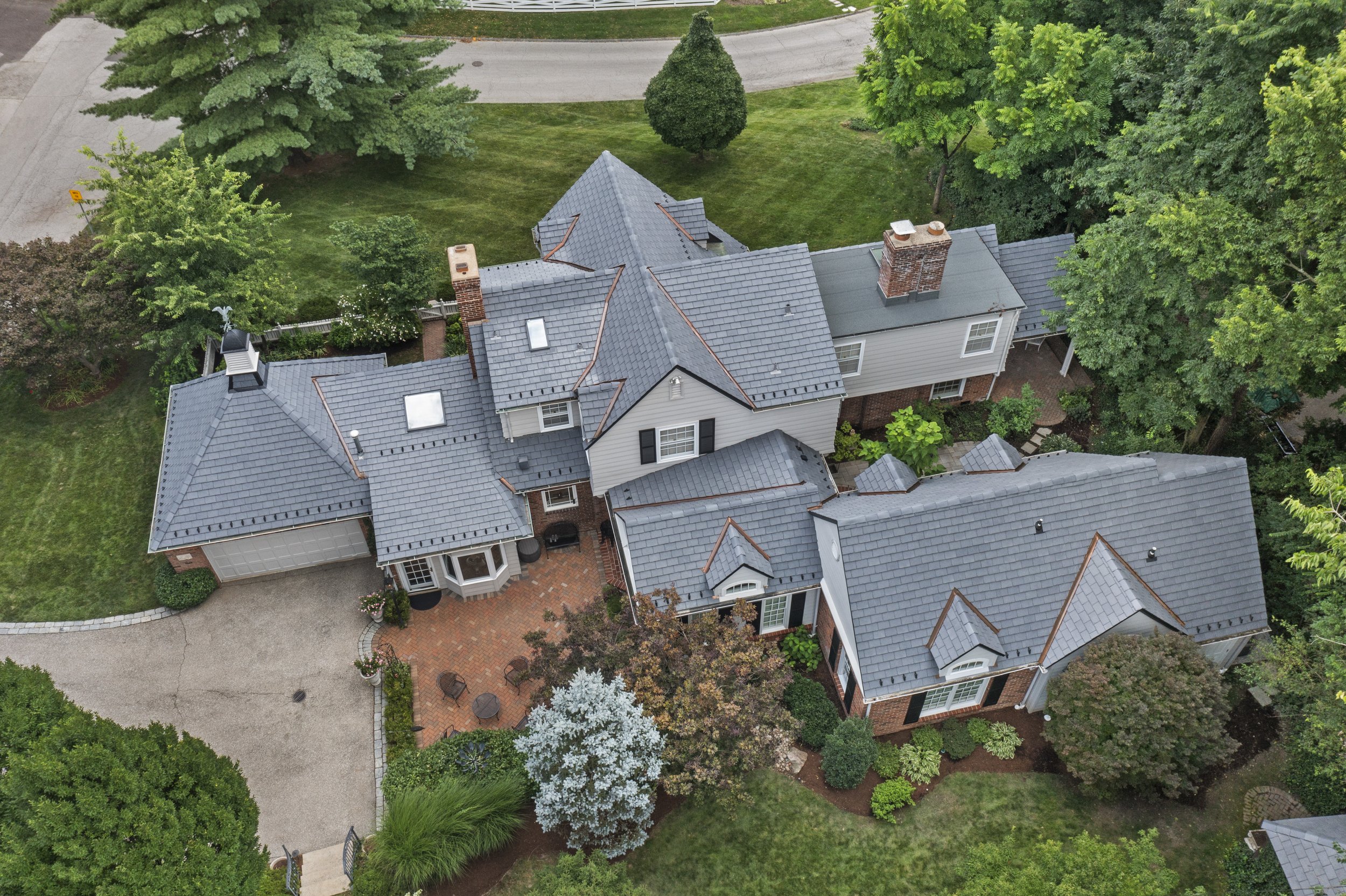 Overhead view of 17 Devon Road showcasing the home's rooflines, brick patios, circular driveway, and landscaped property.