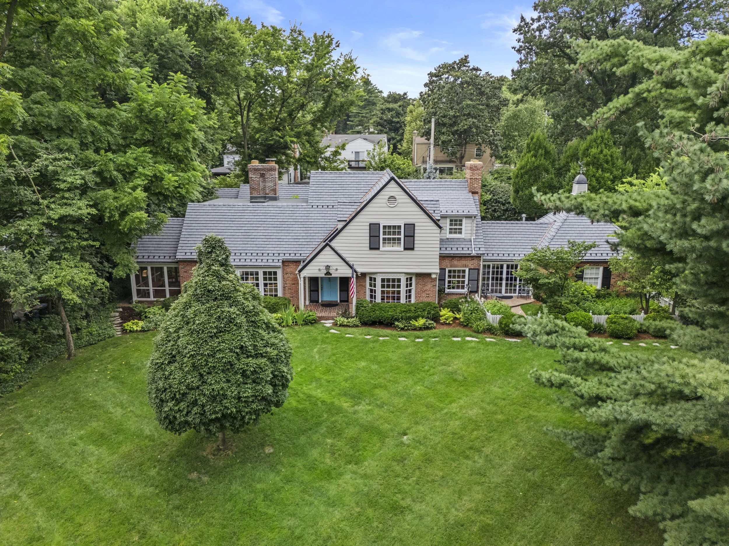 Front exterior of 17 Devon Road featuring expansive lawn, mature landscaping, and brick patio overlooking the backyard.