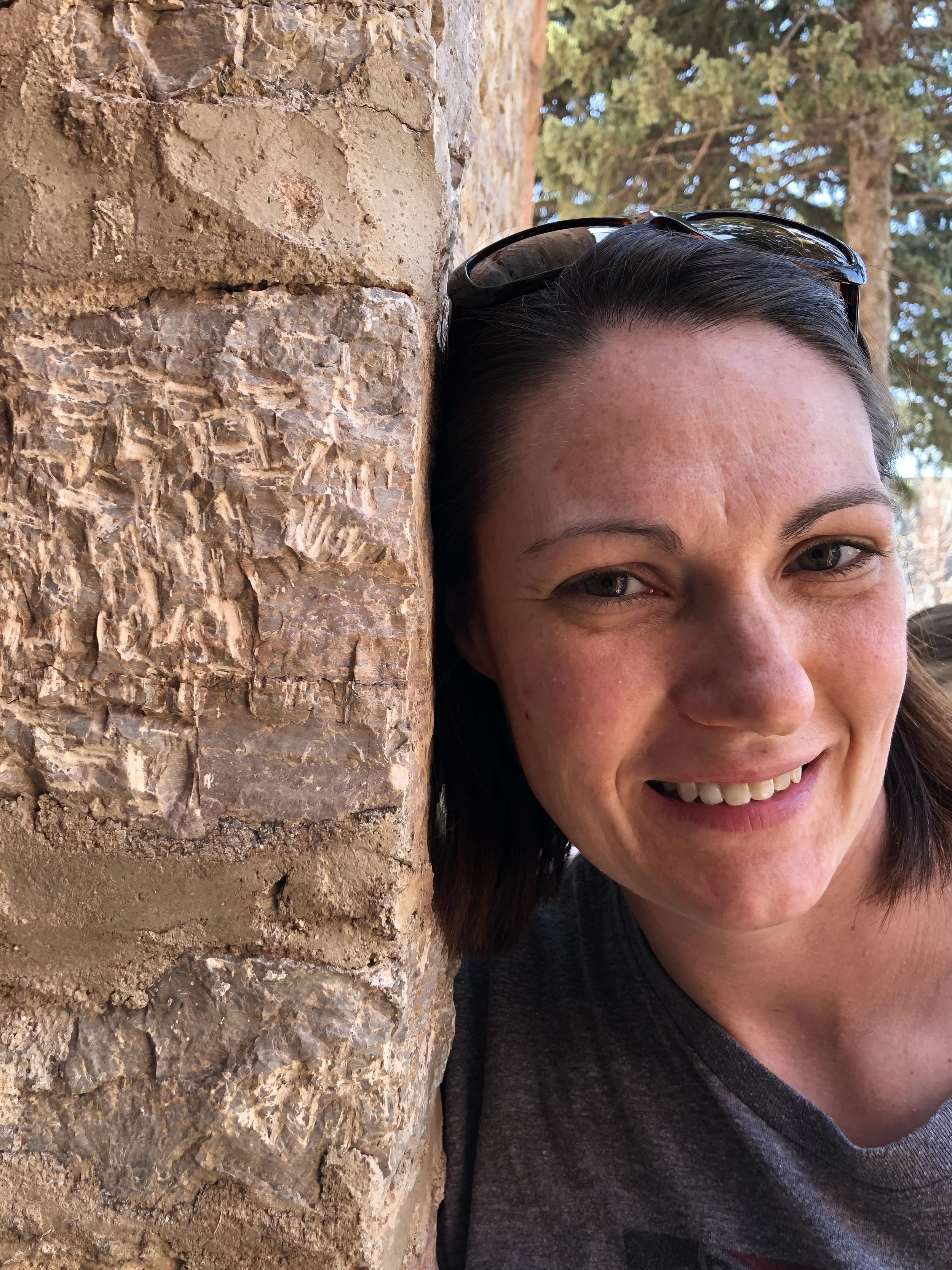 A woman smiling, with only part of her face visible, standing next to a brick wall.