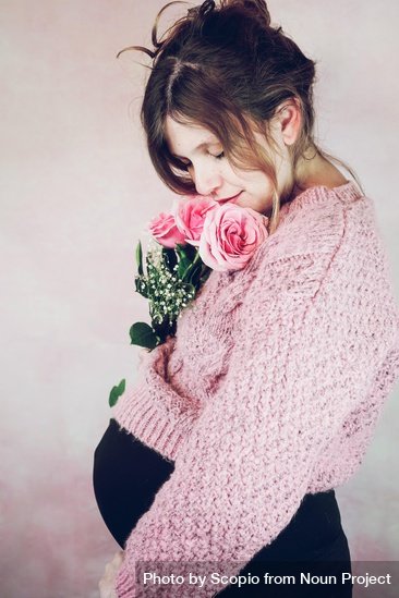 Pregnant woman in a pink sweater holding pink roses against a neutral background.
