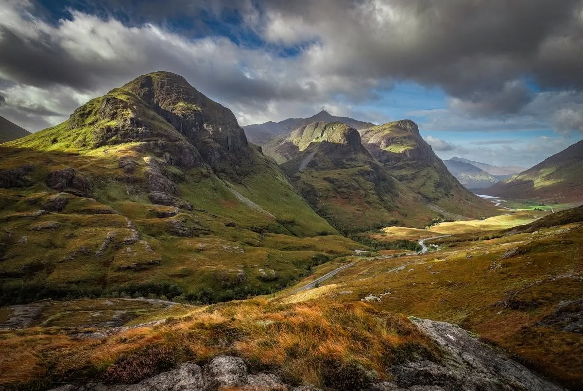 A scenic view of green mountains under a partly cloudy sky with a winding road through a valley.