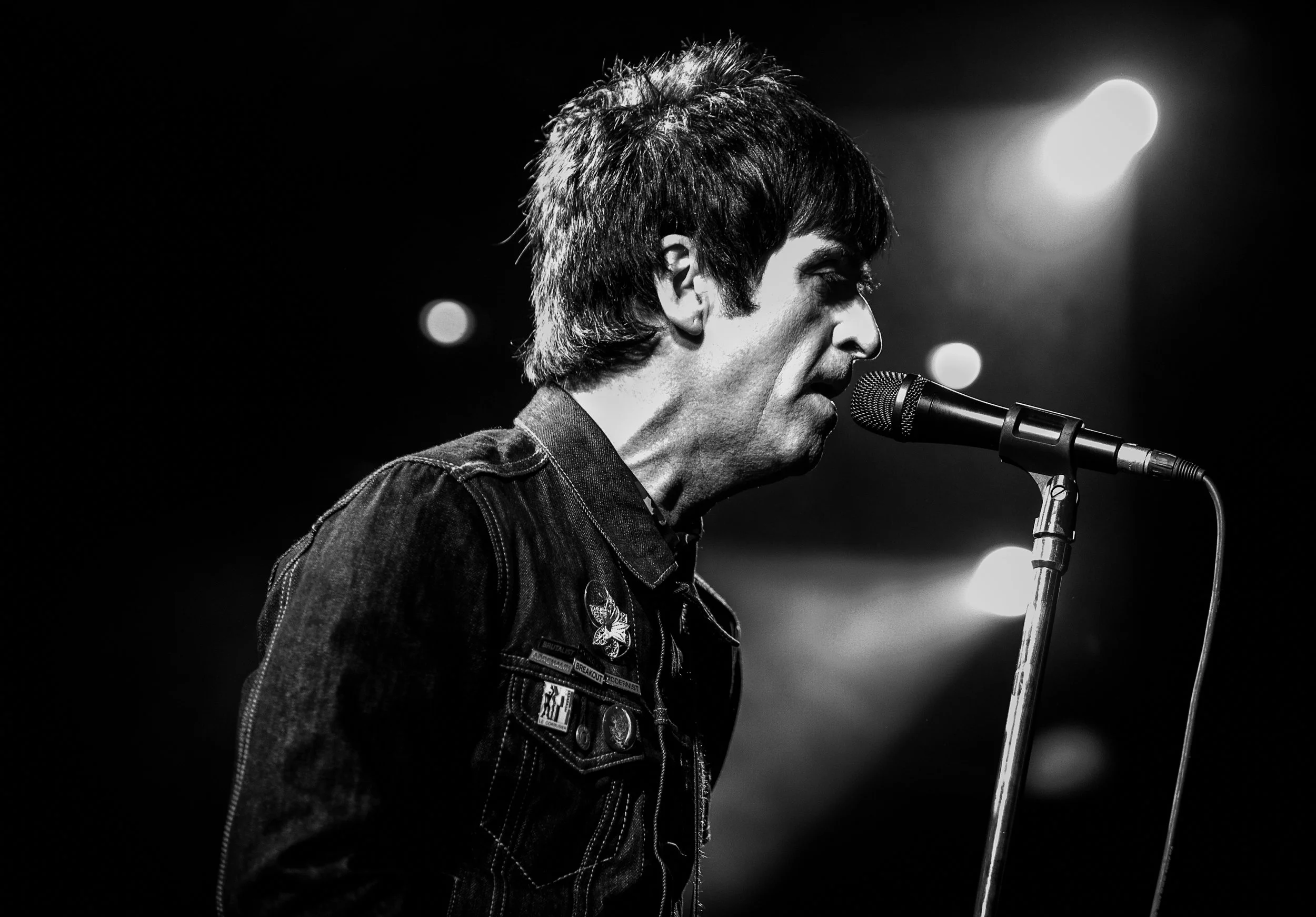 Black and white photo of a man singing into a microphone on stage, with stage lights in the background.