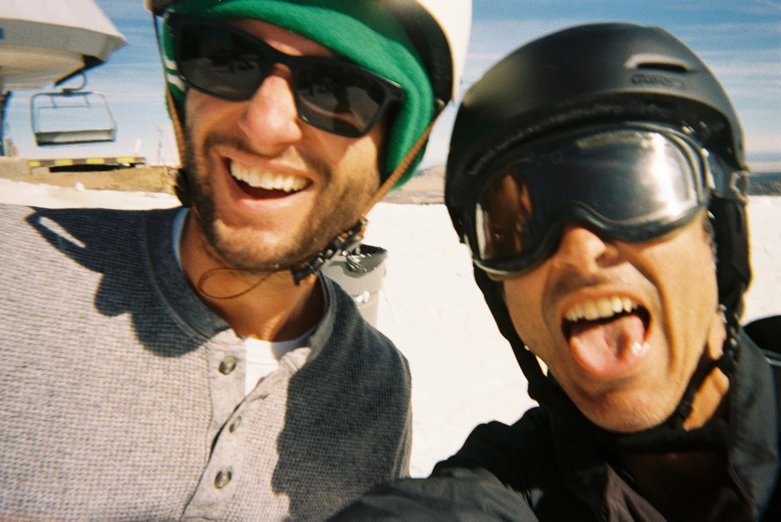 Photo of band members of Breakeven, Angelo and Dan smiling on a mountaintop in helmet and snowboard goggles.