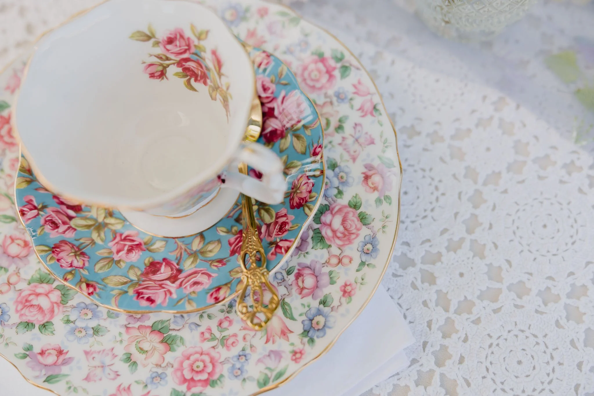 Close-up of three stacked floral patterned porcelain teacups and saucers with gold trim, placed on a lace tablecloth.