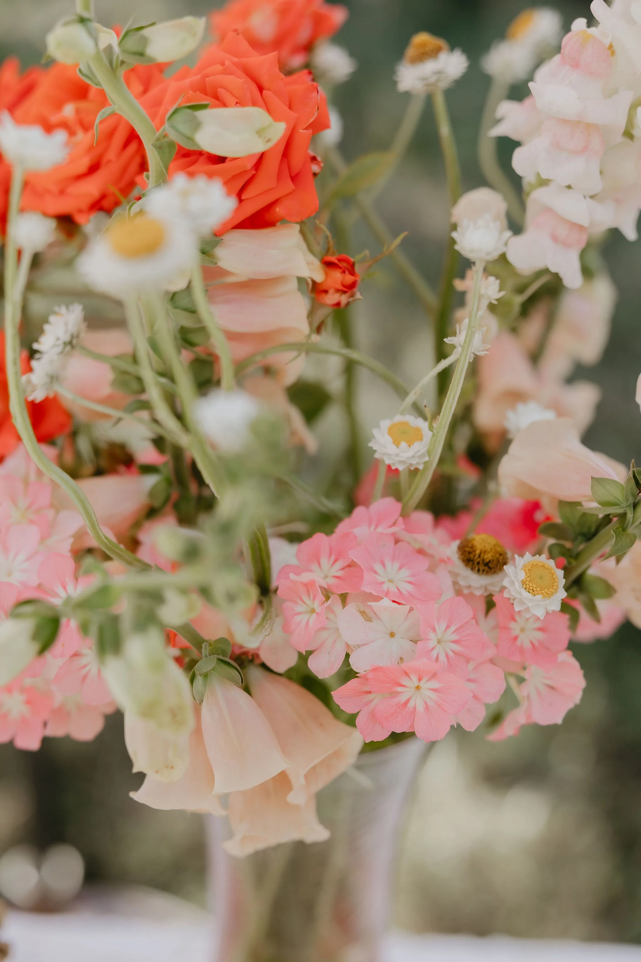 Close-up of a colorful bouquet of flowers with pink, white, and orange blossoms, and green stems.