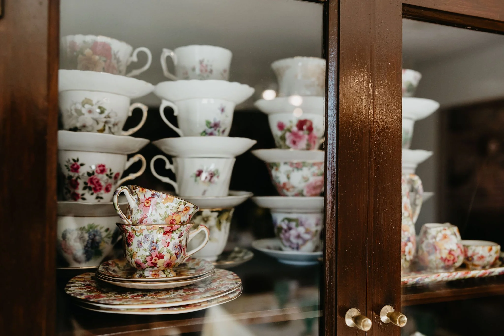 A wooden cabinet with glass doors displaying floral patterned teacups and saucers inside.