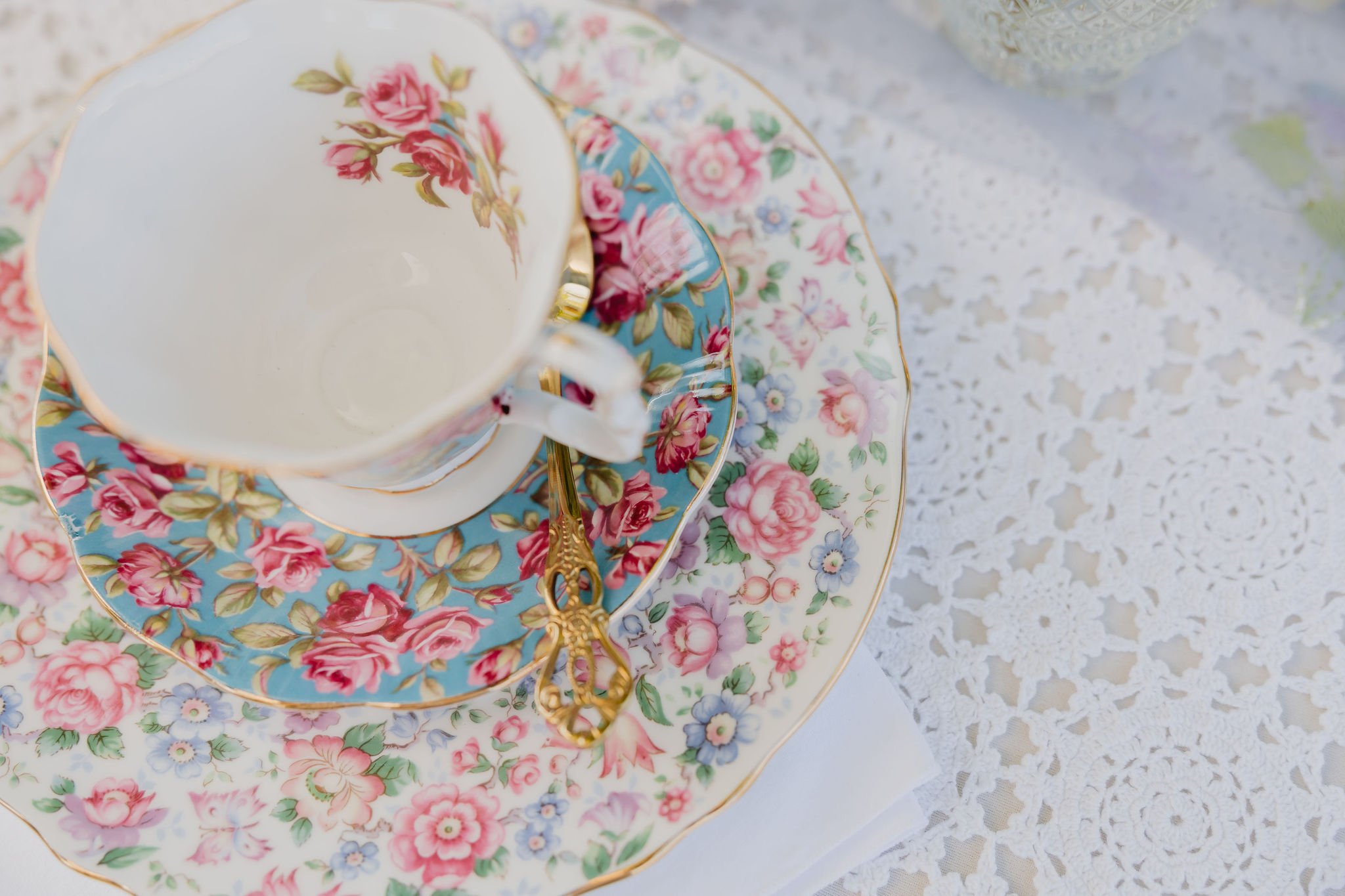 Close-up of vintage floral patterned teacup and saucer with gold trim on a lace tablecloth.