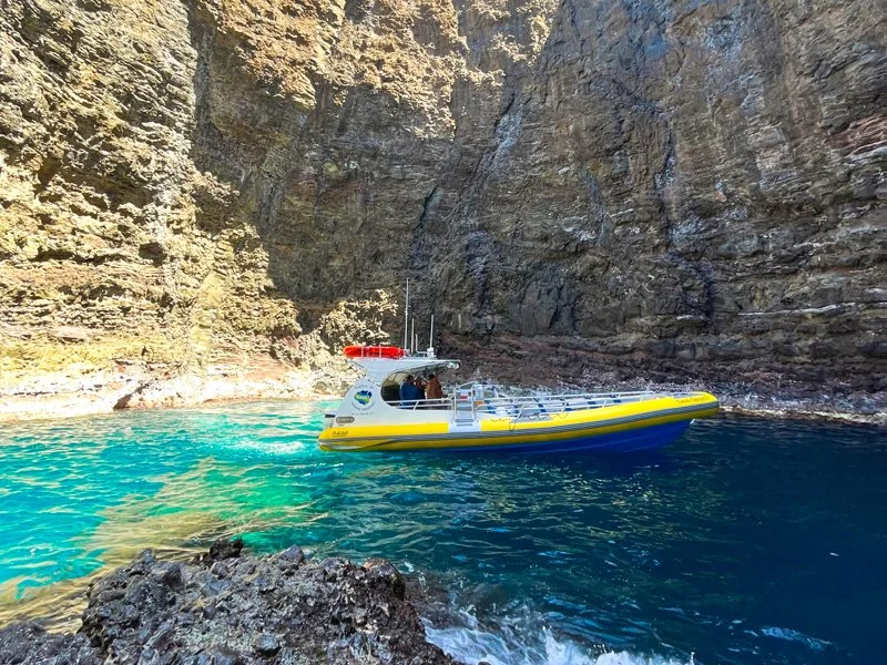 A yellow and white boat navigating through a narrow canyon with rocky walls, in turquoise water.